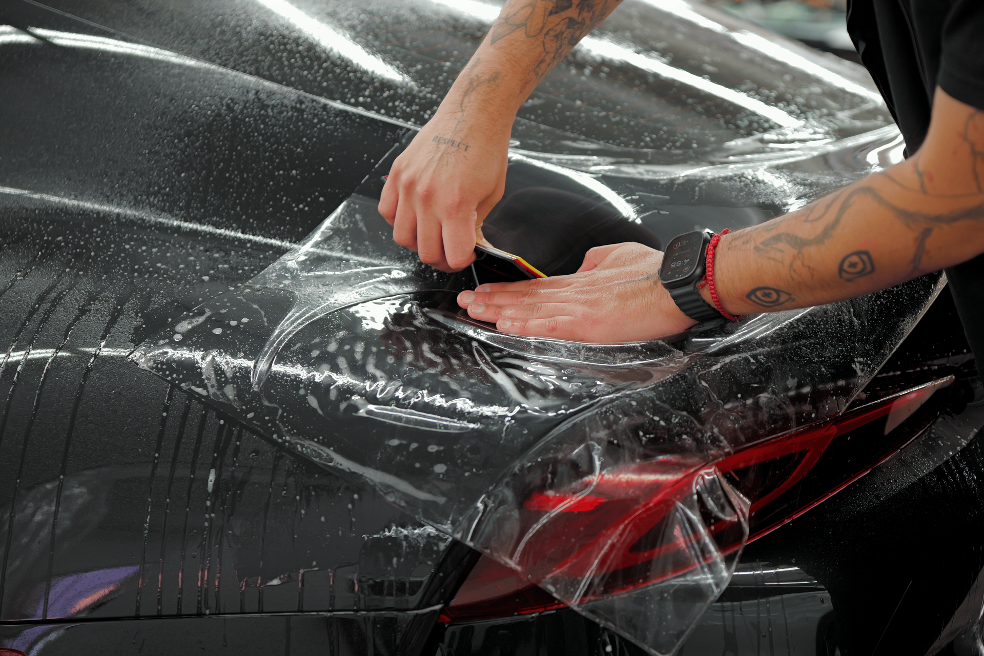 Hands using a squeegee to apply blue vinyl wrap to a car door