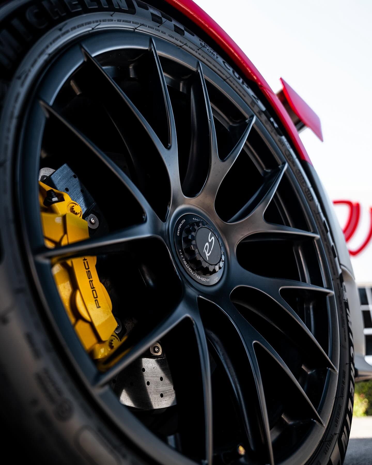 Close-up of a black multi-spoke car wheel with a yellow brake caliper on a red sports car