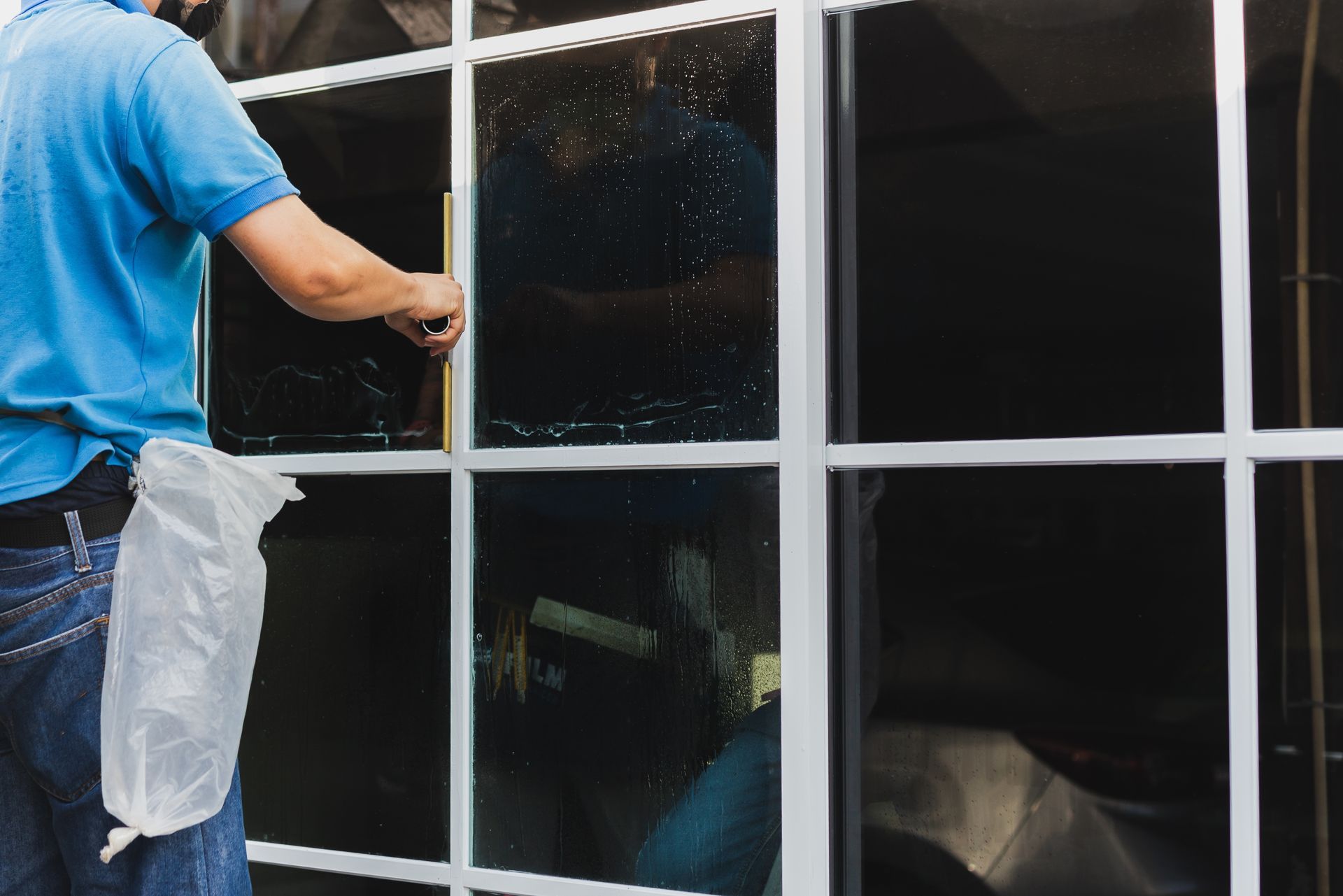 Person cleaning a window with a squeegee, white cloth, and spray bottle outdoors