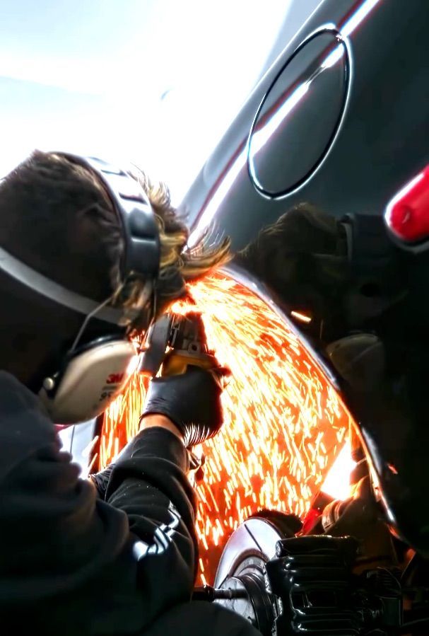 Person using a grinder to cut metal on a black car, sending bright sparks downward