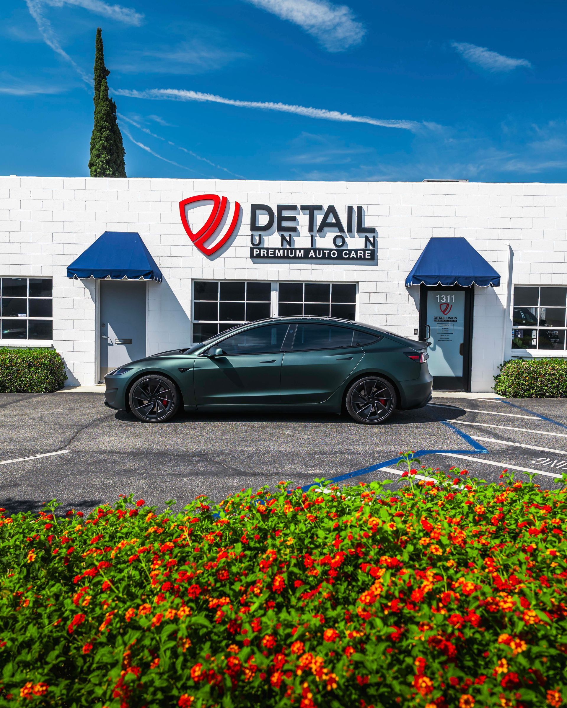 Black sedan parked outside a Detail Boutique storefront with blue awnings and flower bed in front