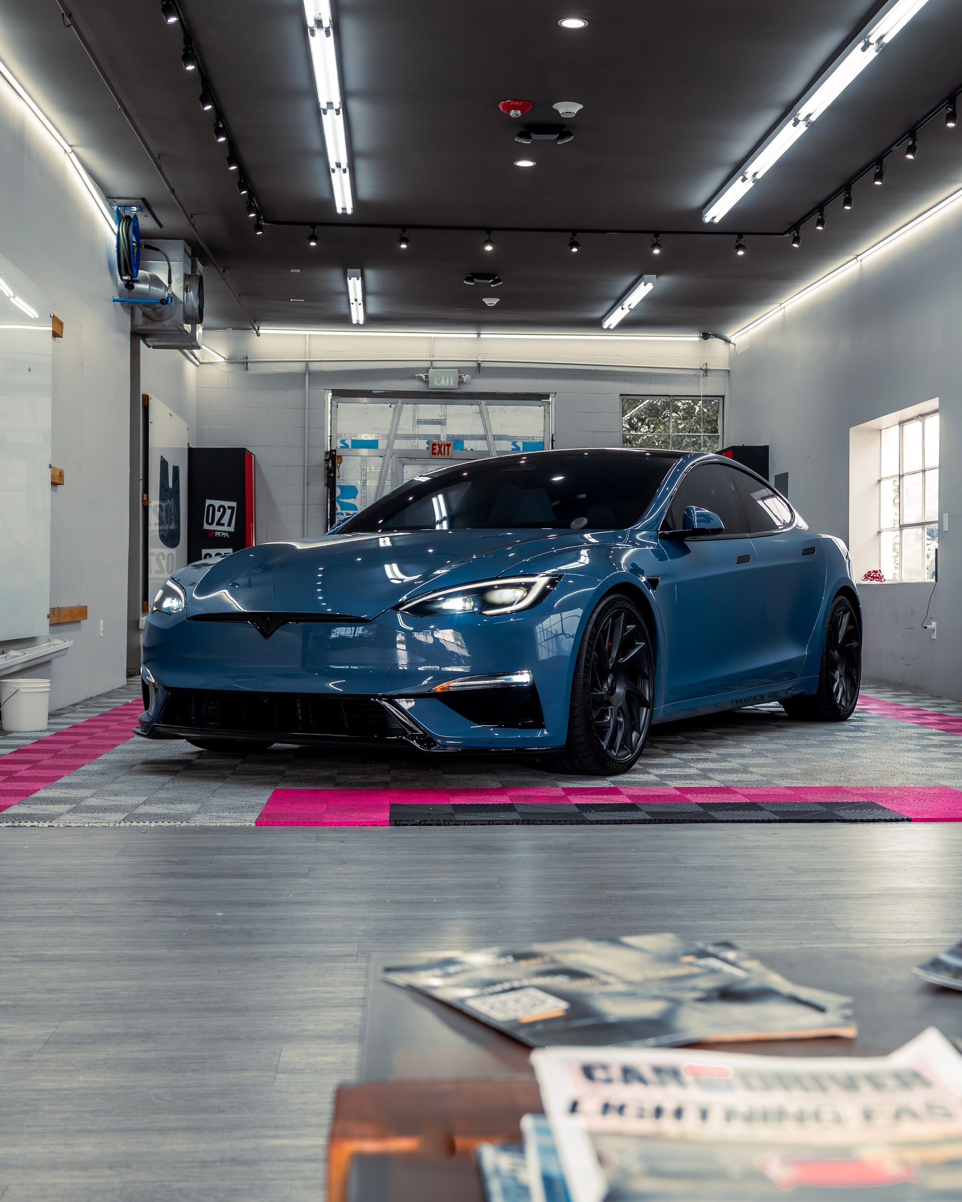 Hands applying liquid to a blue sports car’s front fender in a workshop