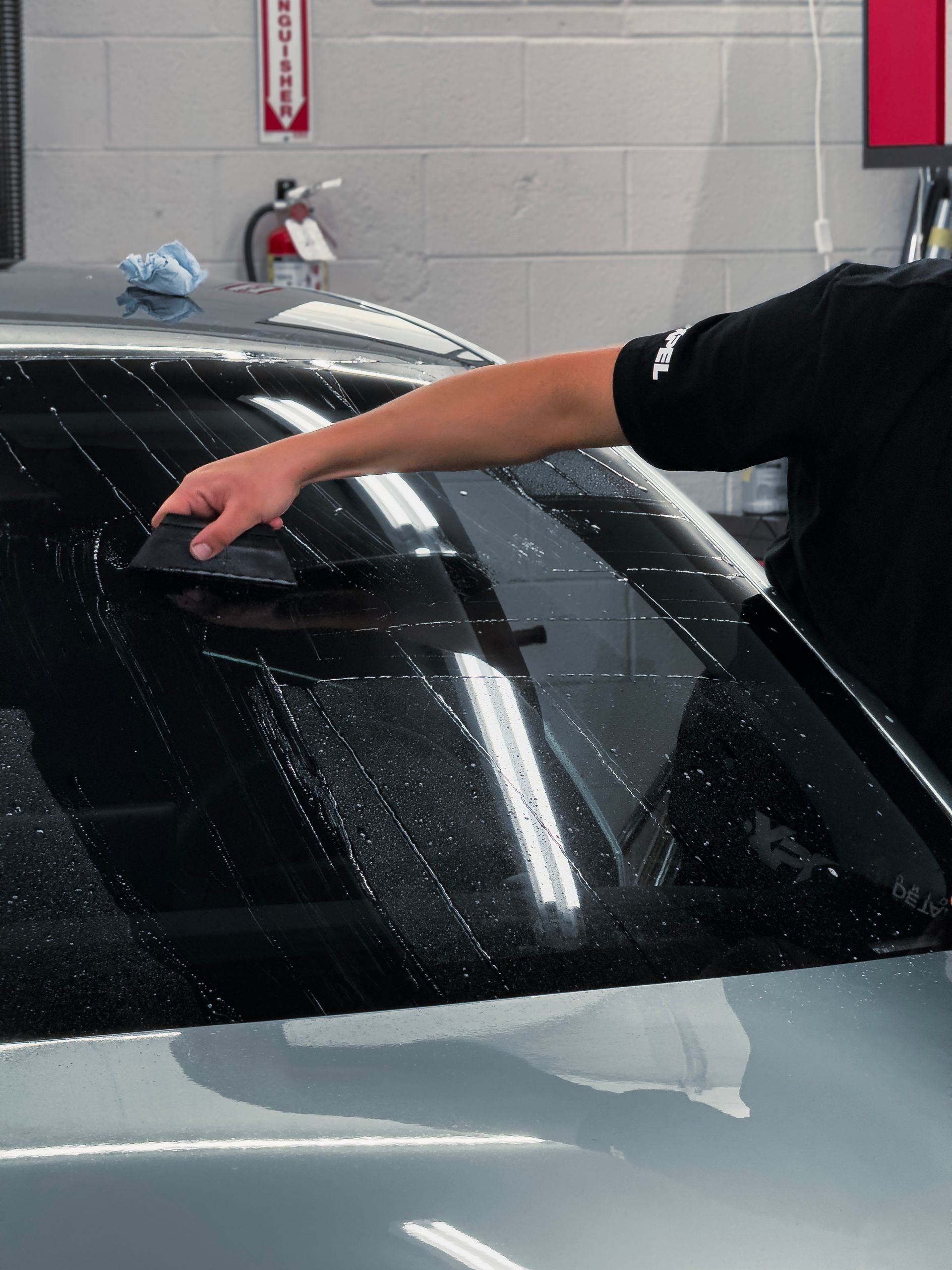 Person wiping the rear windshield of a black car in a car wash bay