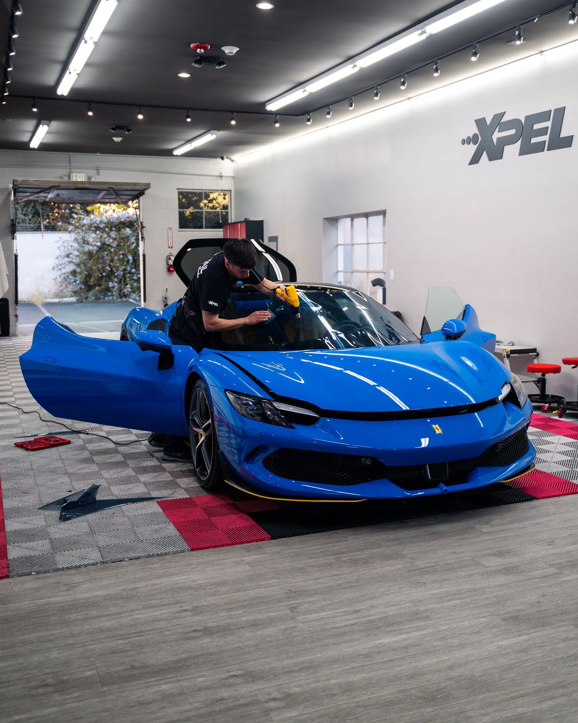 Hands applying liquid to a blue sports car’s front fender in a workshop
