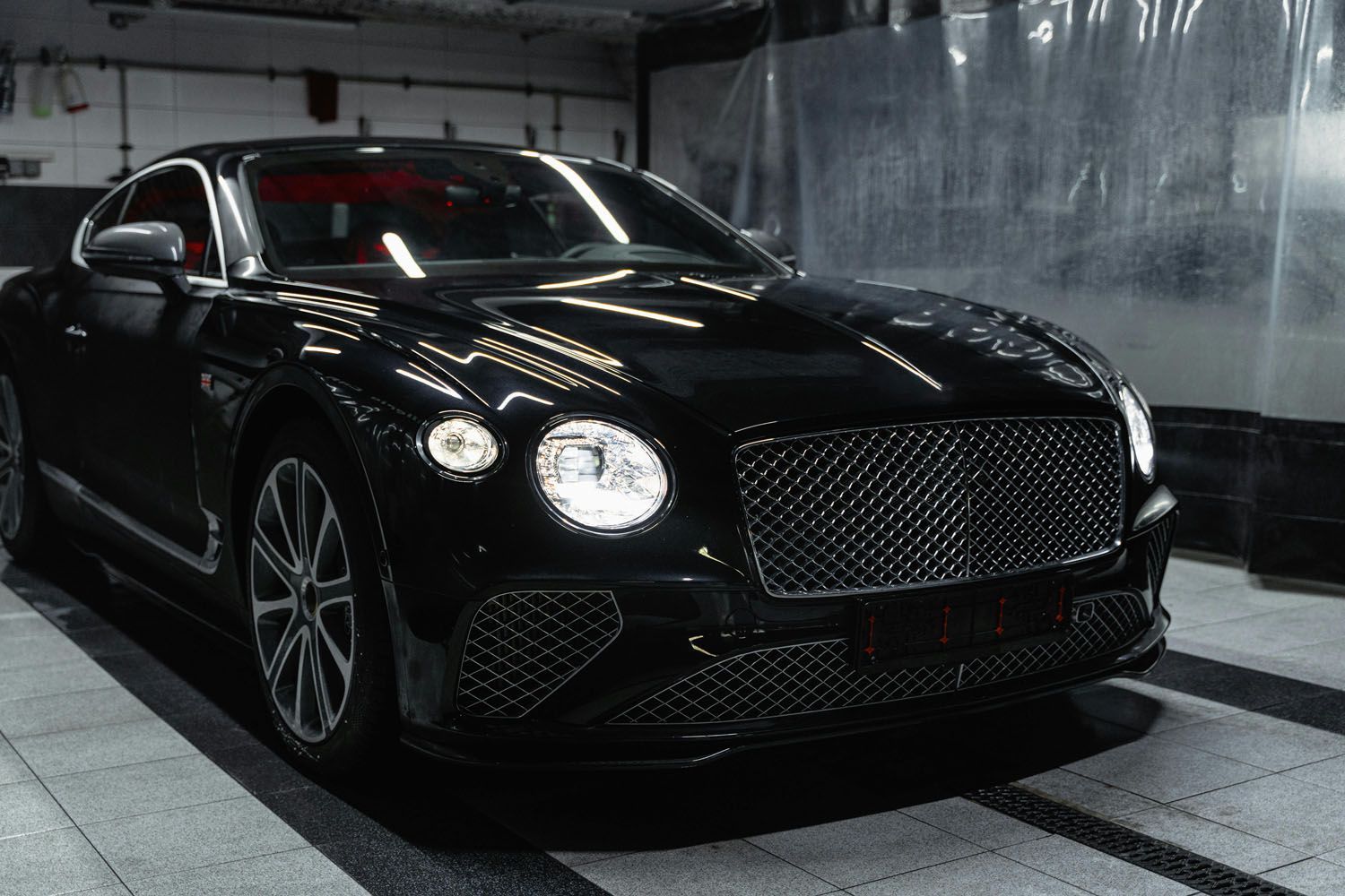 Black luxury coupe parked in a dim garage, front-left view with headlights on