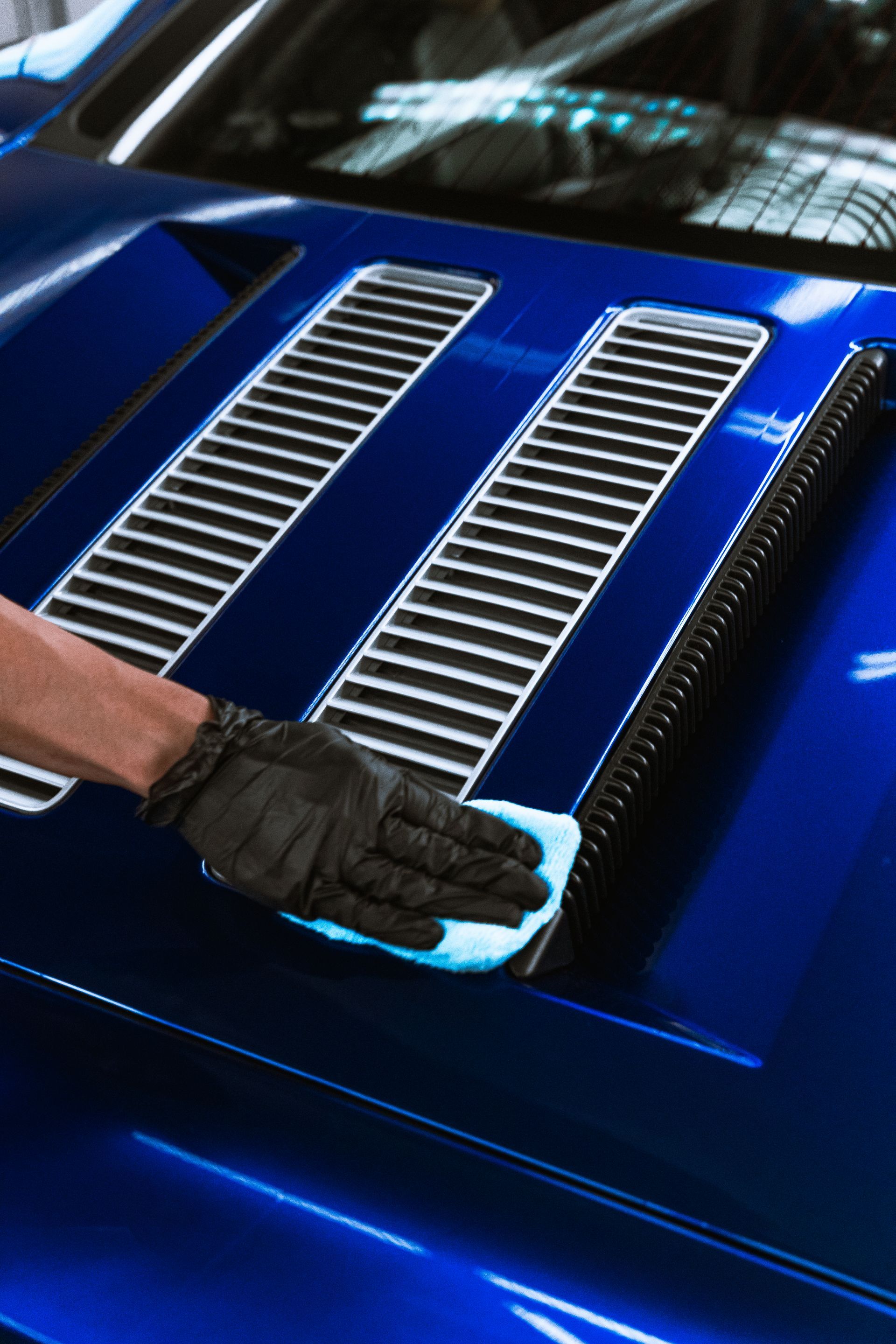 Gloved hand polishing a blue car hood with silver vents