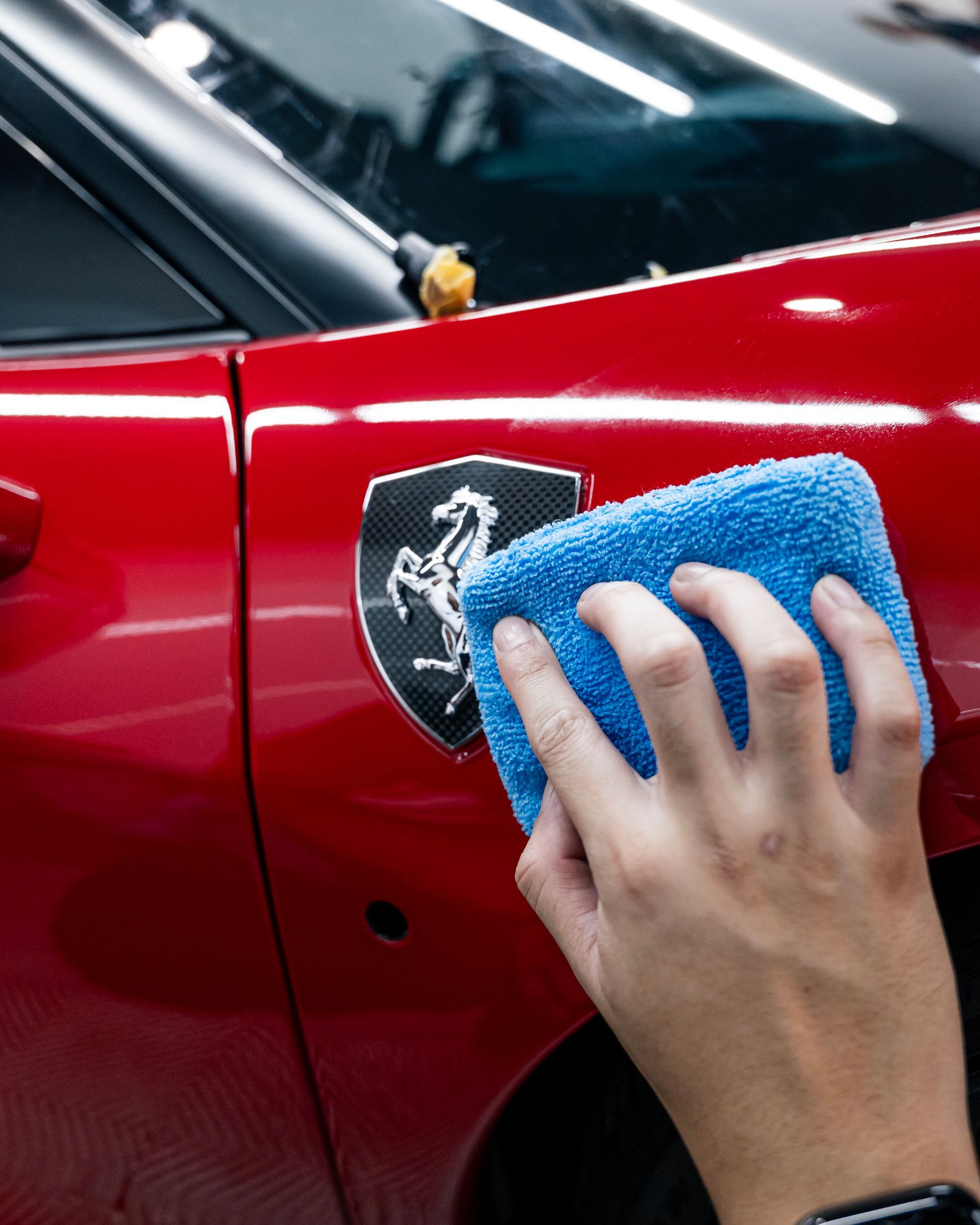 Hand wiping a red car door with a blue cloth near a Ferrari badge