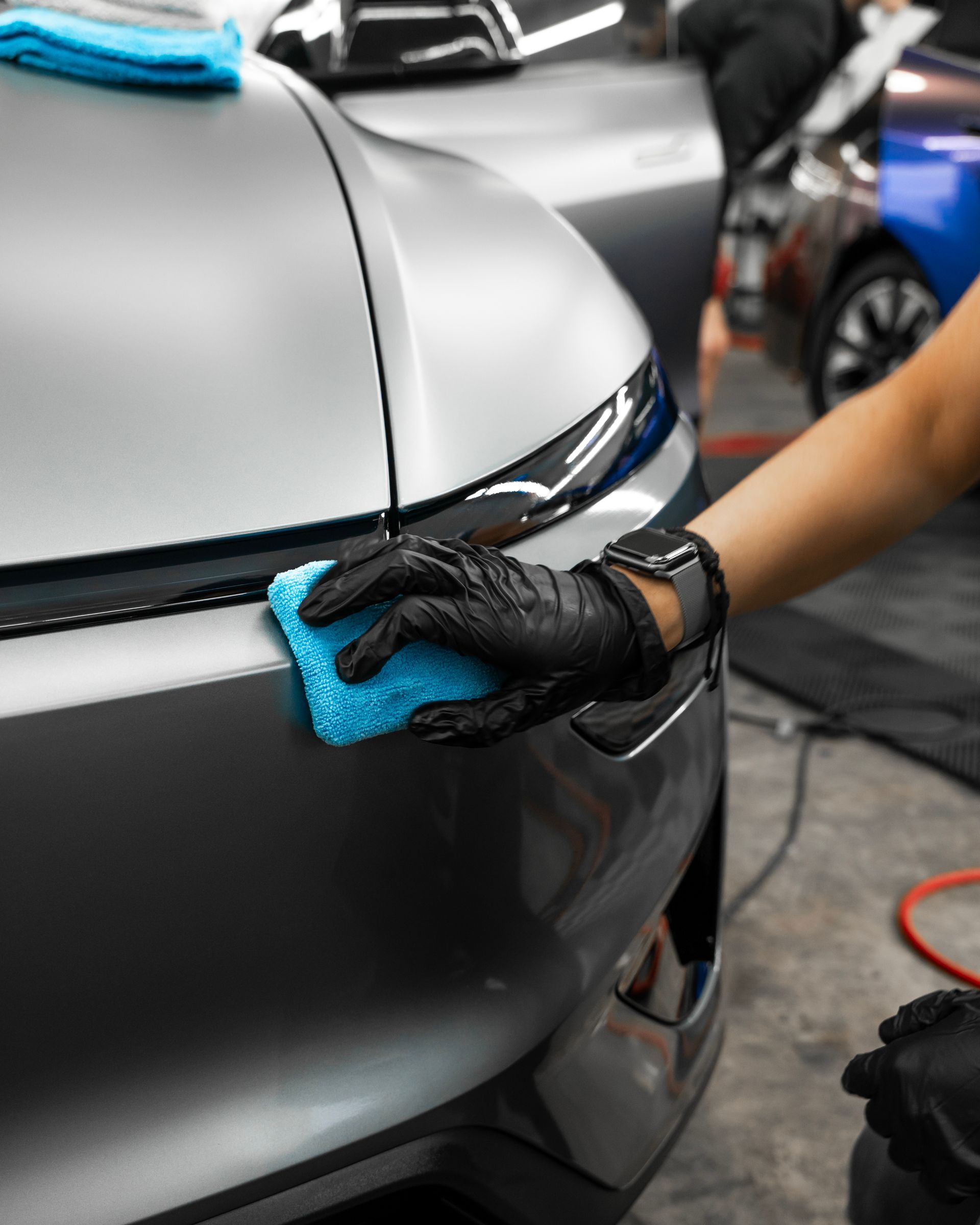 Gloved hand wiping a black car bumper with a blue cloth in a auto detailing shop