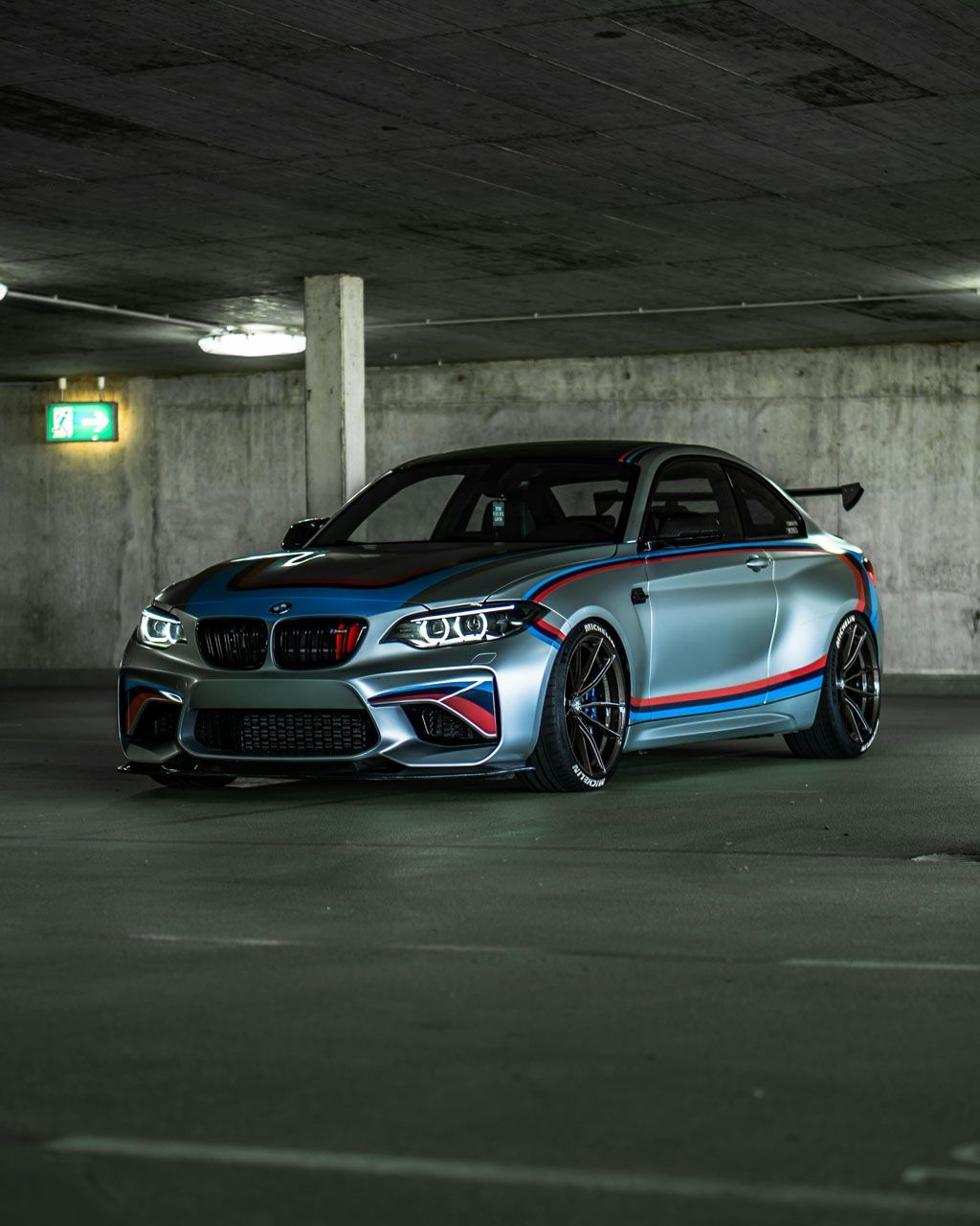 Modified silver-and-black sports sedan parked in a dim concrete parking garage, with red and blue accents.