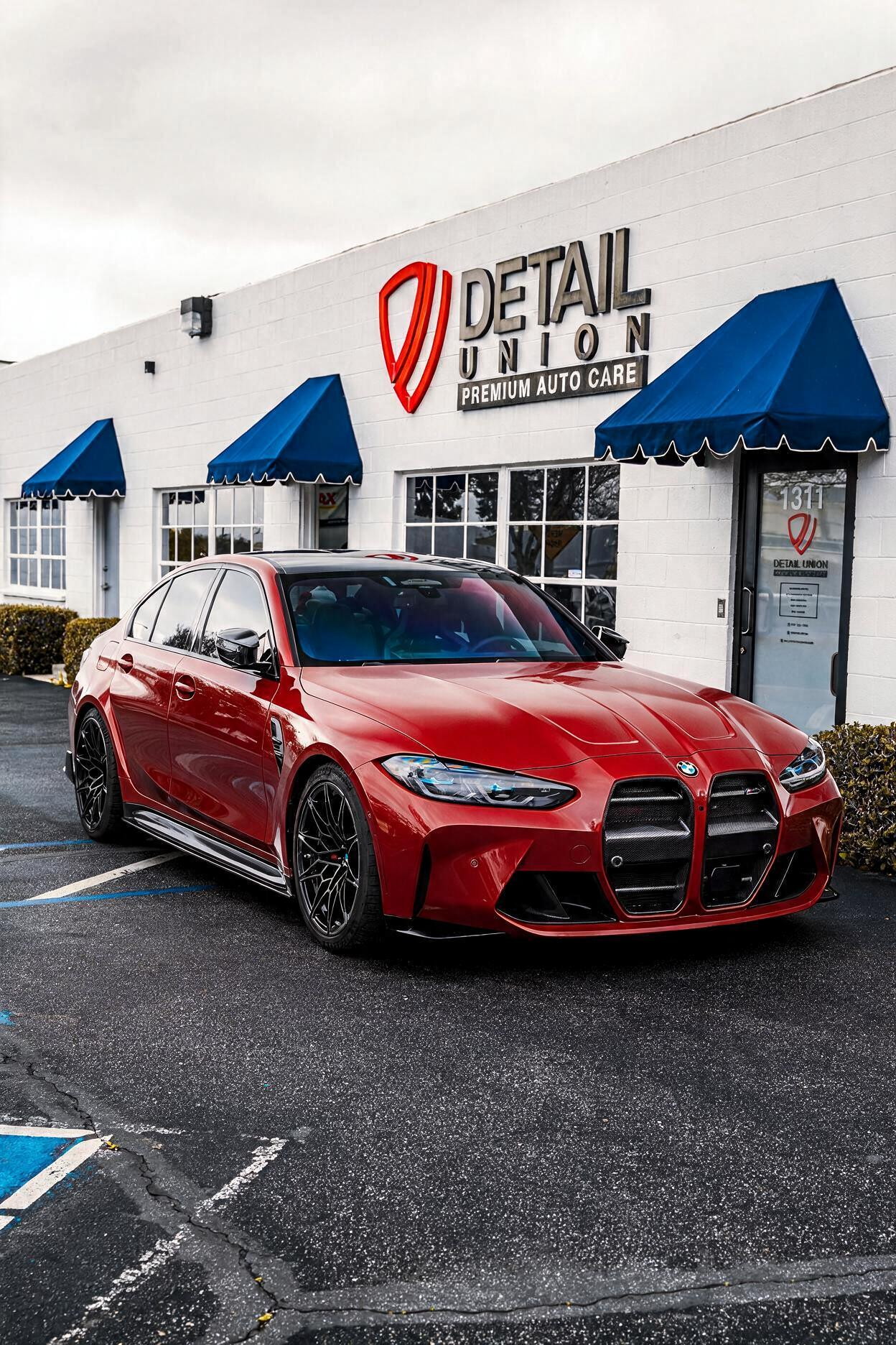 Red sports sedan parked outside Detail Garage, with blue awnings and wet pavement