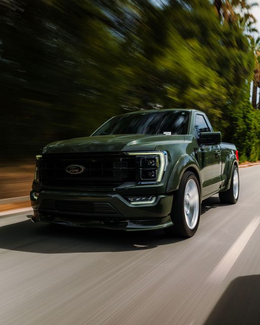 Dark green pickup truck driving on a sunlit road with trees blurred in the background