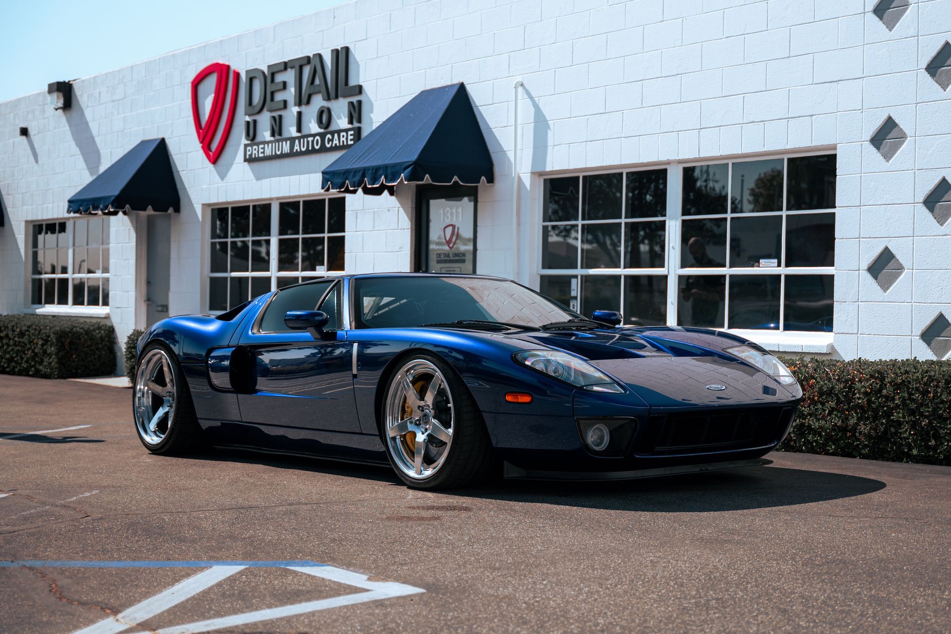 Blue sports car parked outside a detail shop with awnings and large windows