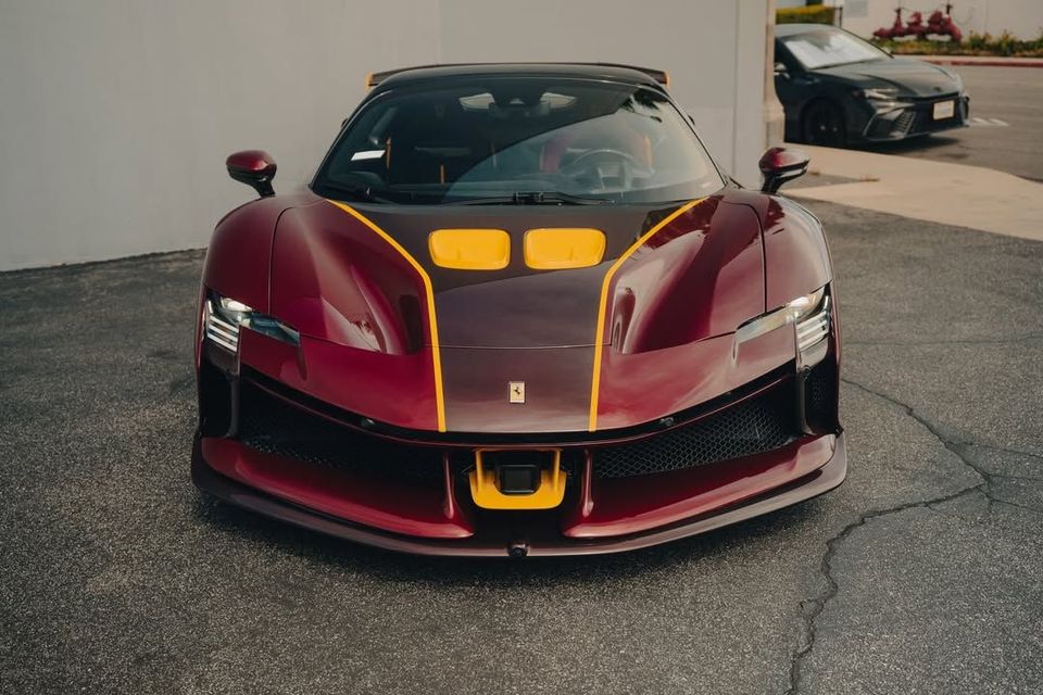 Front view of a maroon sports car with yellow accents parked on pavement