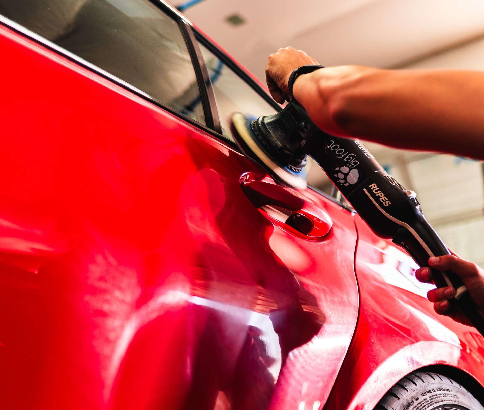 Person polishing a red car with a buffer in a garage