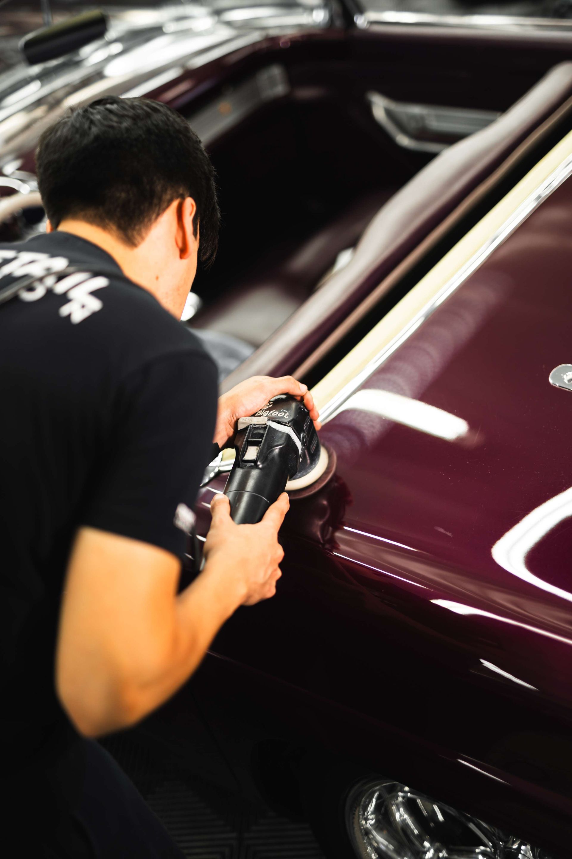 Hands applying liquid to a blue sports car’s front fender in a workshop