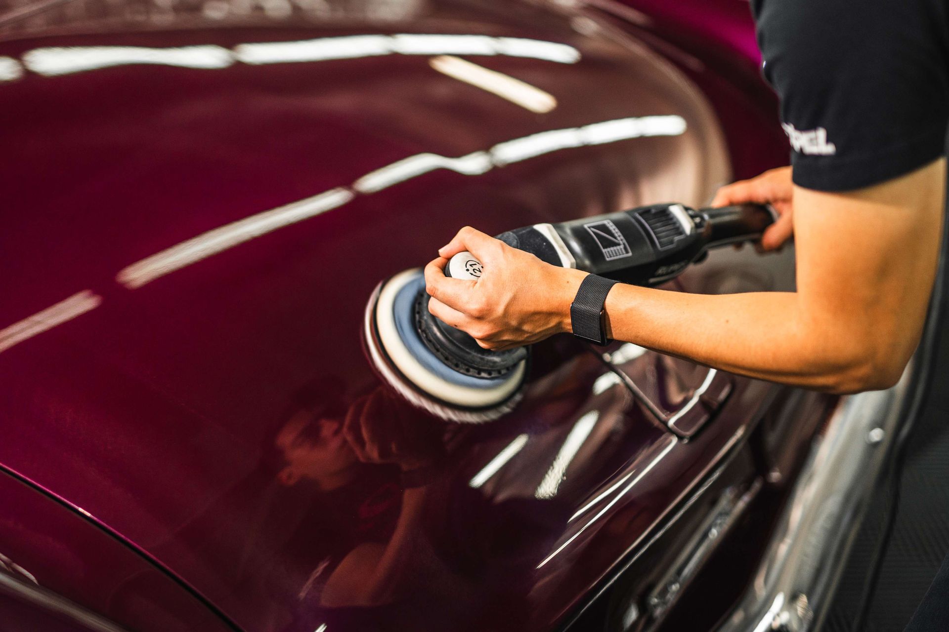 Person polishing a maroon car door with a buffer in a garage
