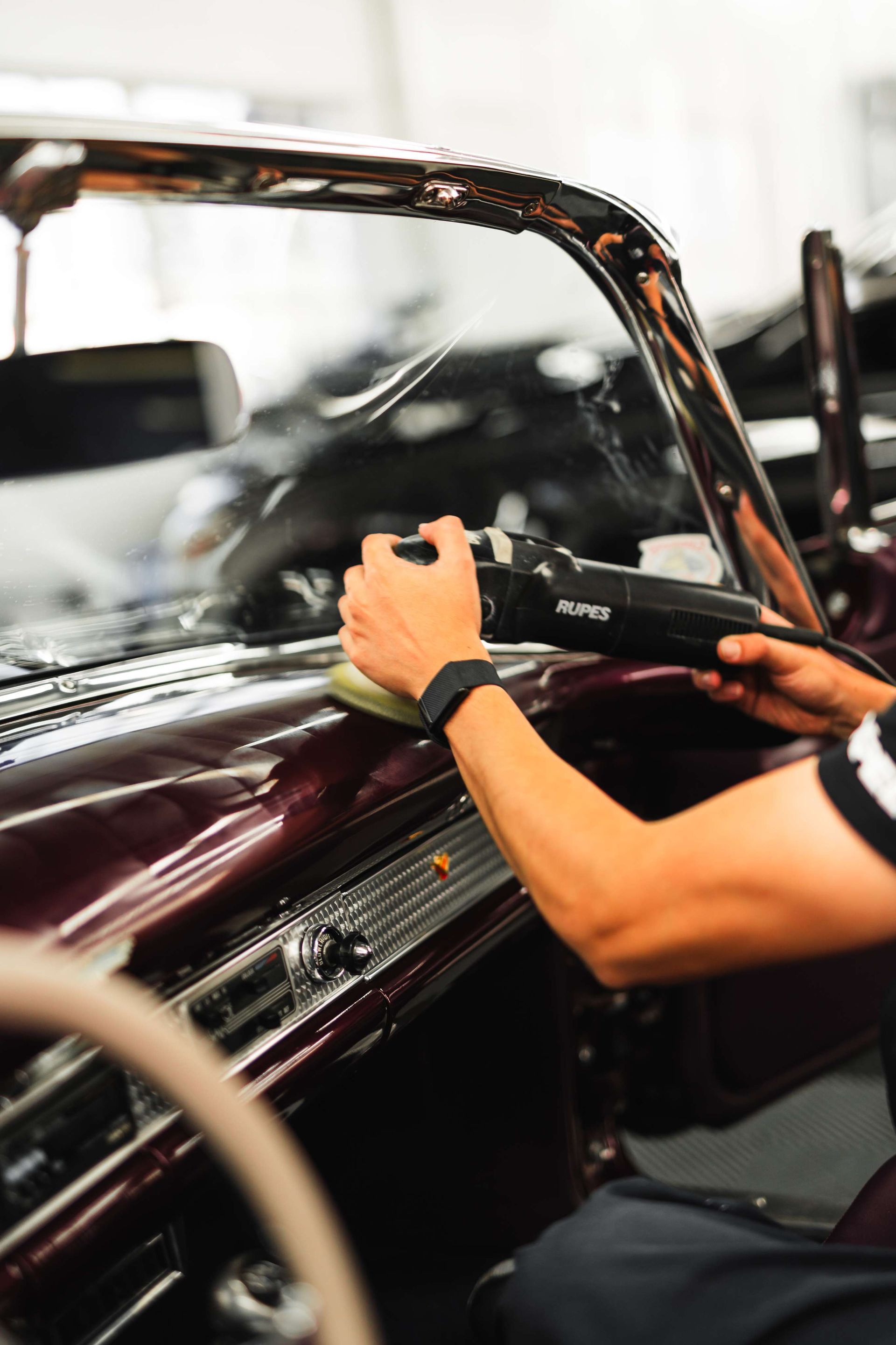 Person using a power tool to work on a maroon car body in an auto shop