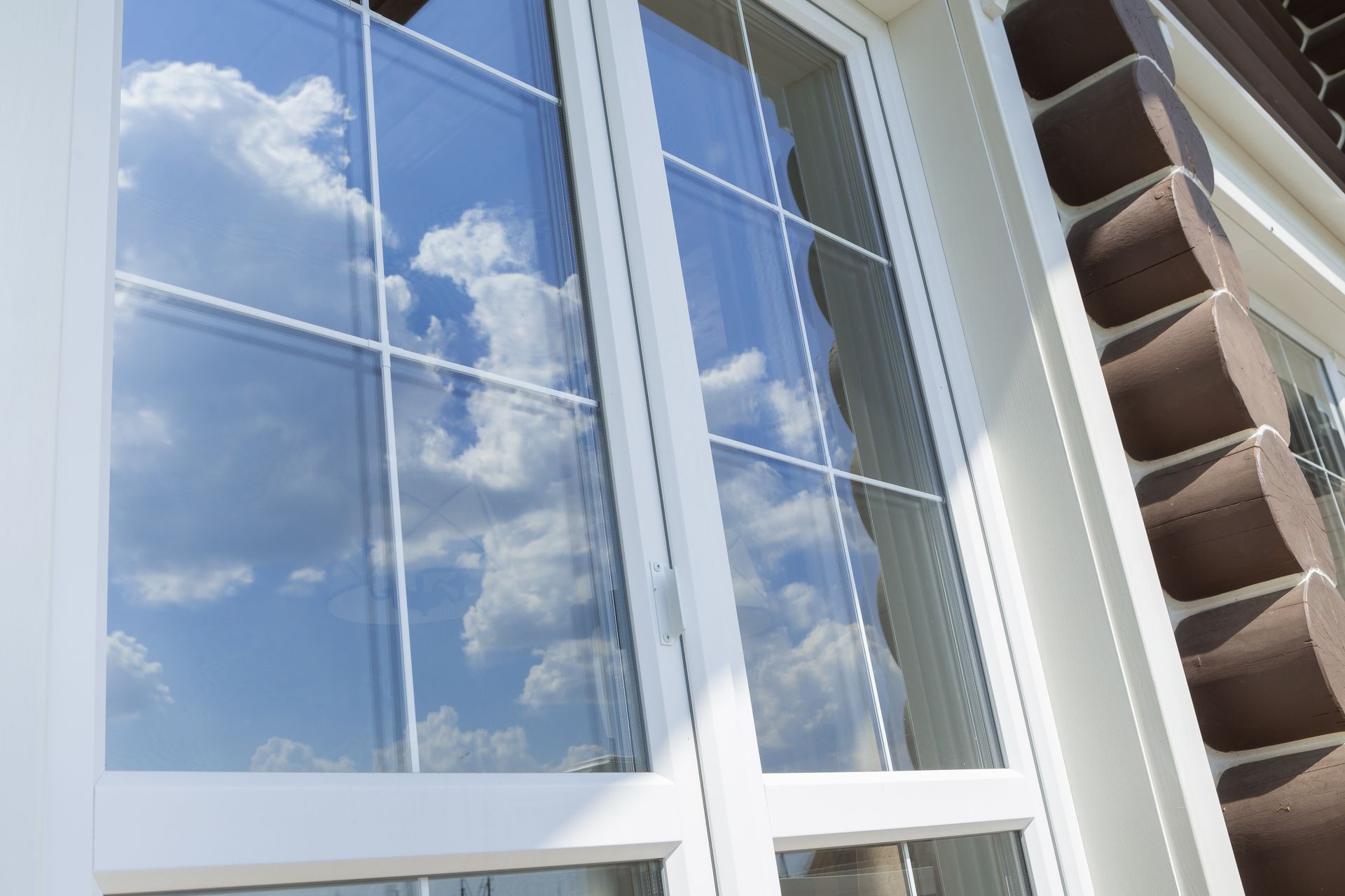 White-framed window reflecting blue sky and clouds beside tan house siding