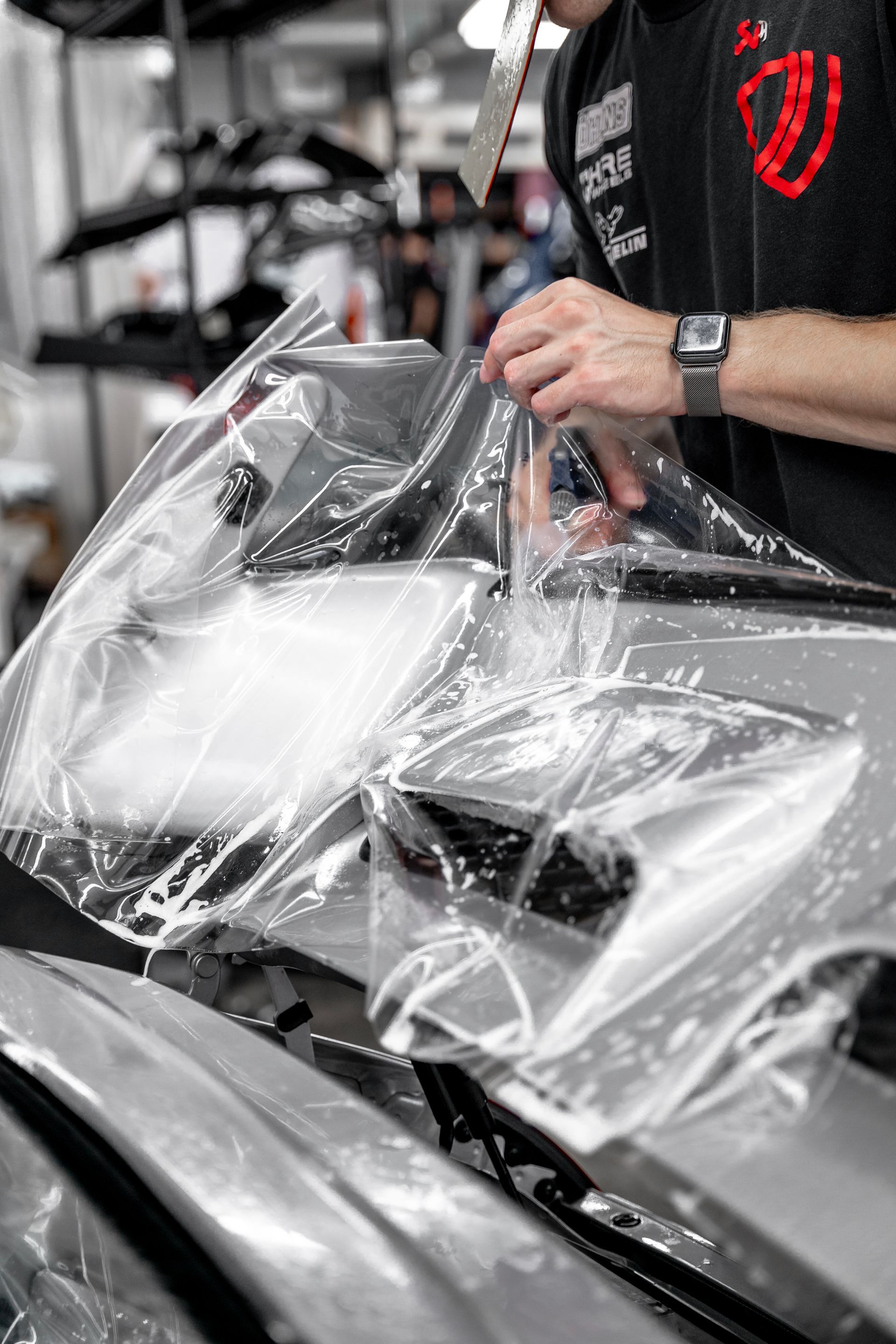 Hands applying liquid to a blue sports car’s front fender in a workshop