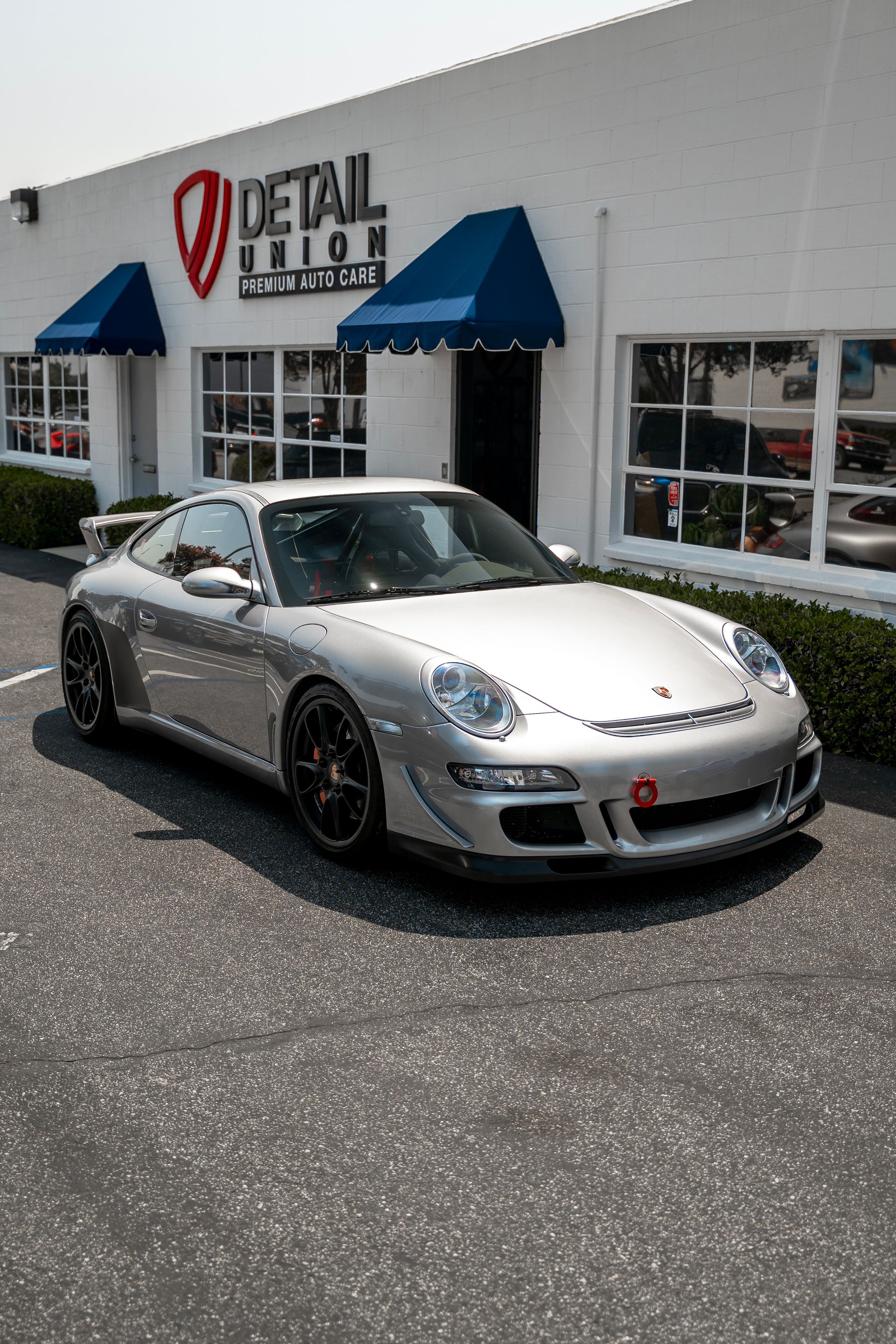 Brown Porsche parked outside a Detail Union shop with black awnings