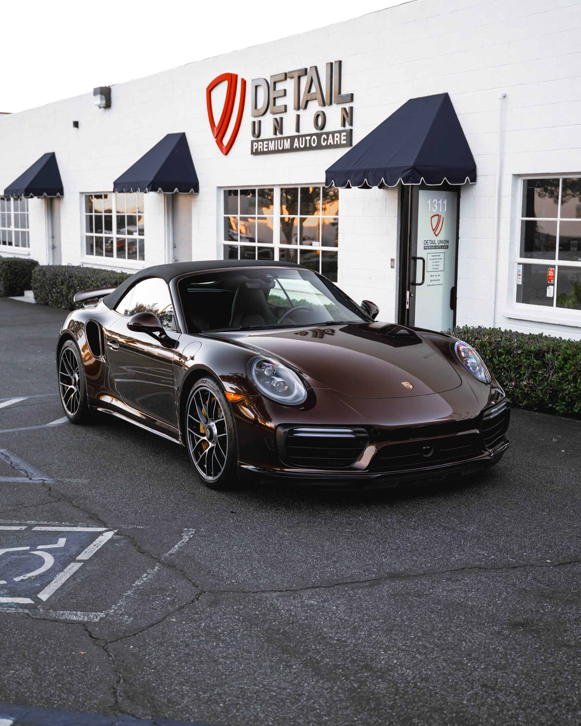 Brown Porsche parked outside a Detail Union shop with black awnings