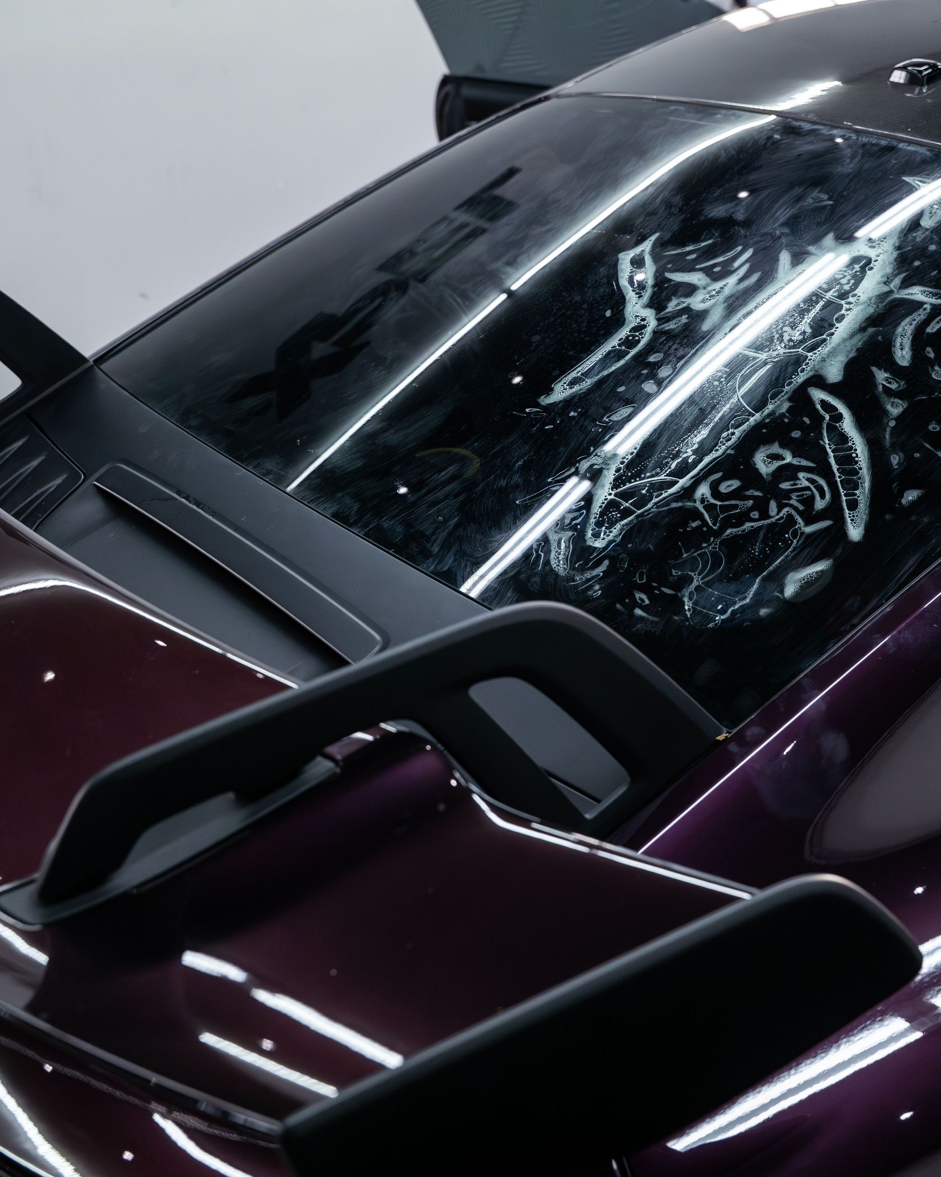 Hands applying liquid to a blue sports car’s front fender in a workshop