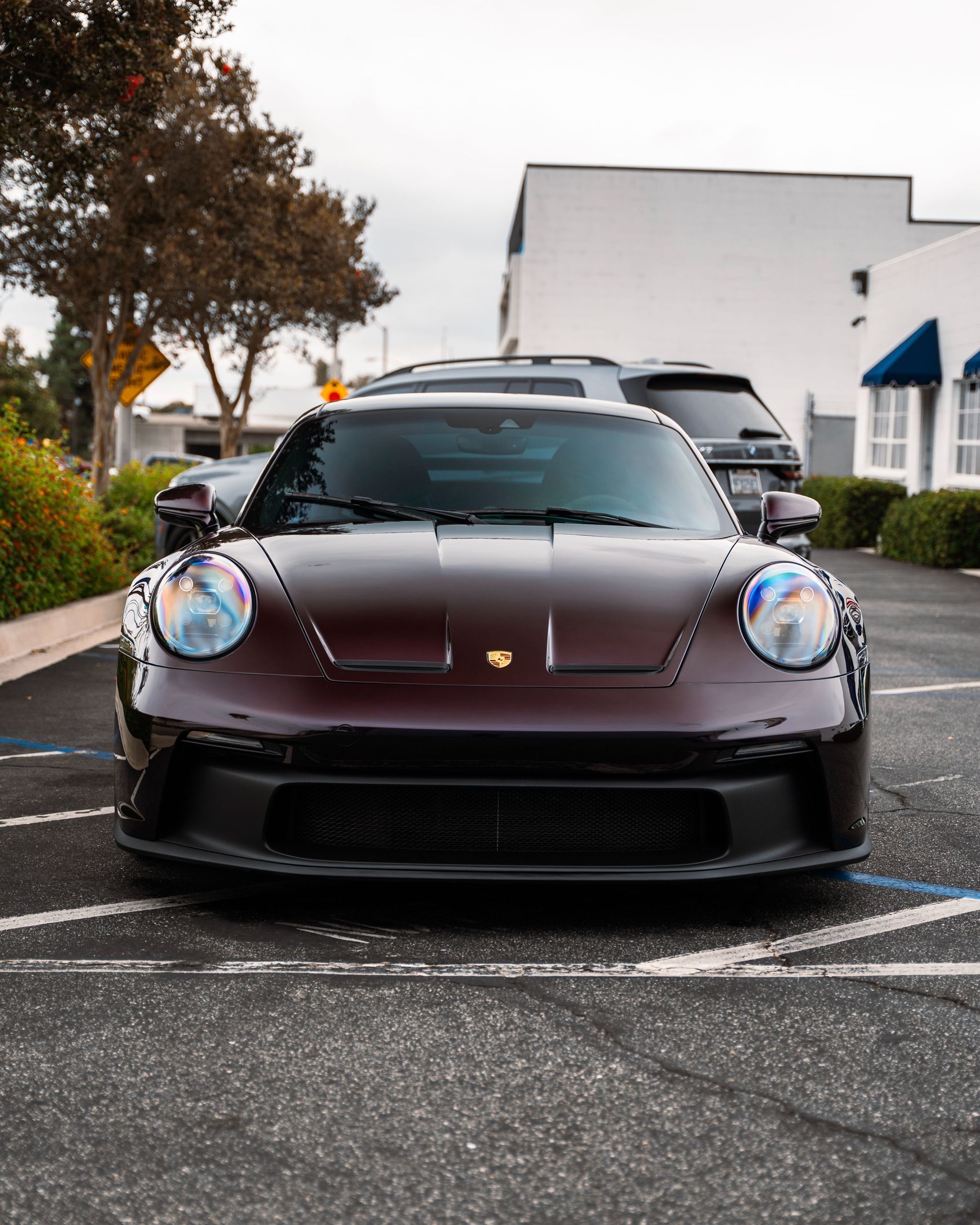 Maroon Porsche sports car parked on a wet street outside white buildings and trees