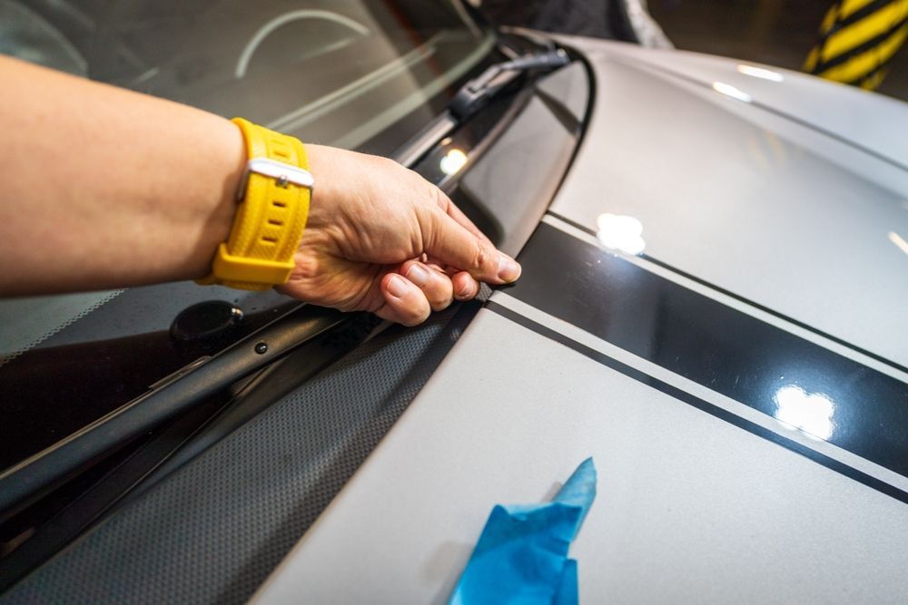 Hand scraping tint film from a car windshield with a blue squeegee