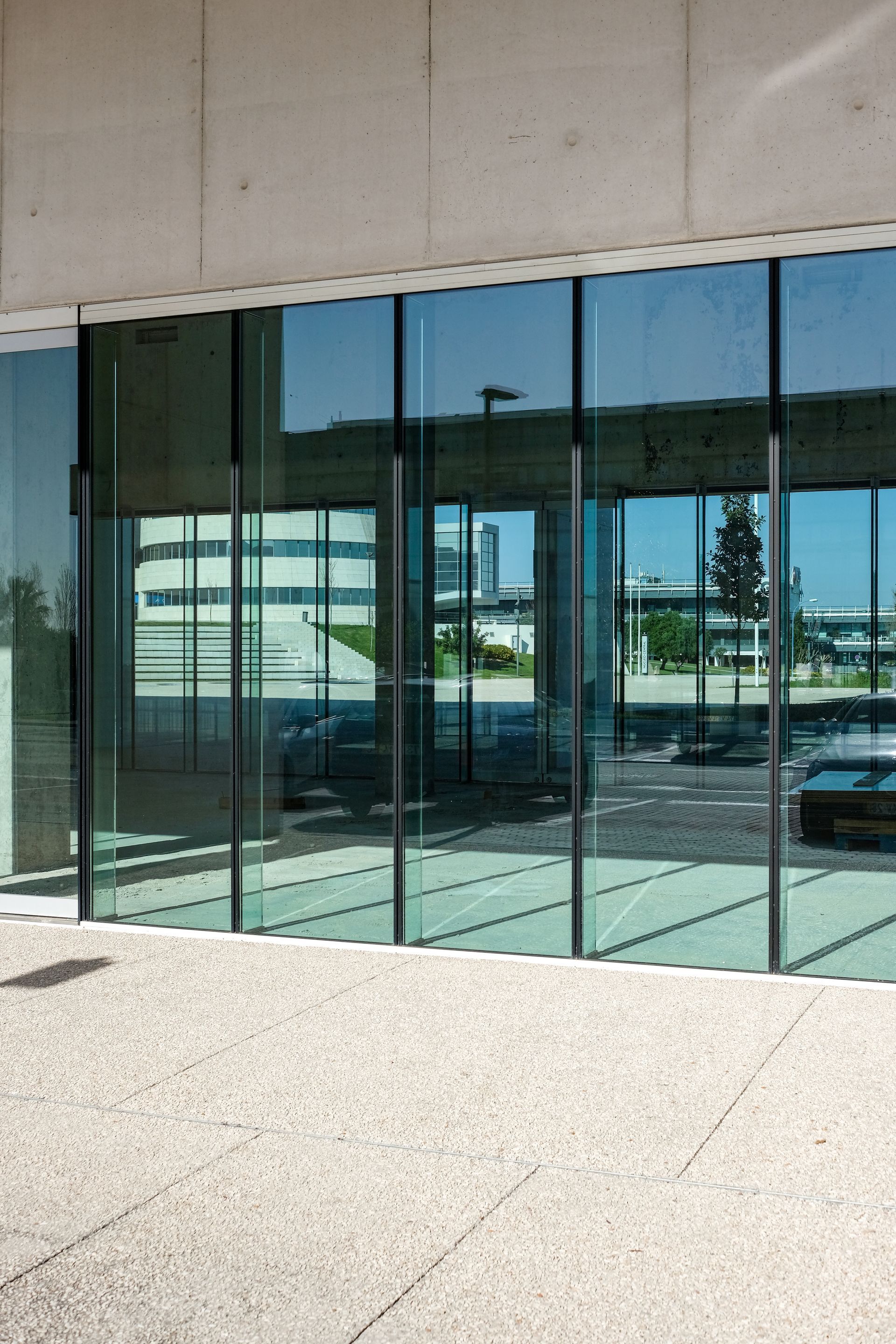 Glass-fronted modern building entrance with reflective windows and a concrete walkway