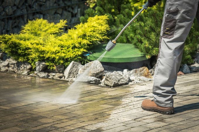 Person pressure washing a brick patio.