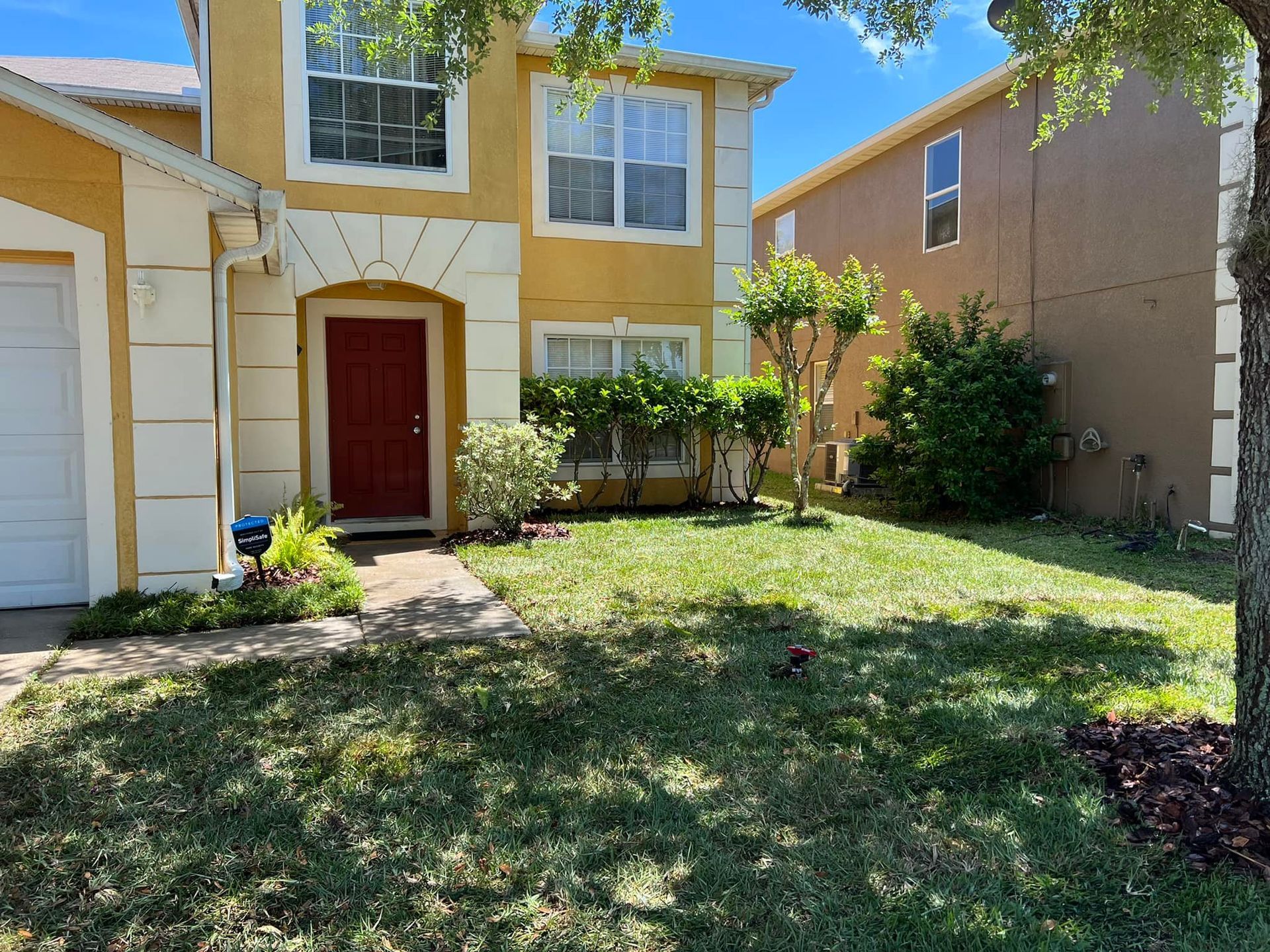 Yellow house with red door and green lawn.