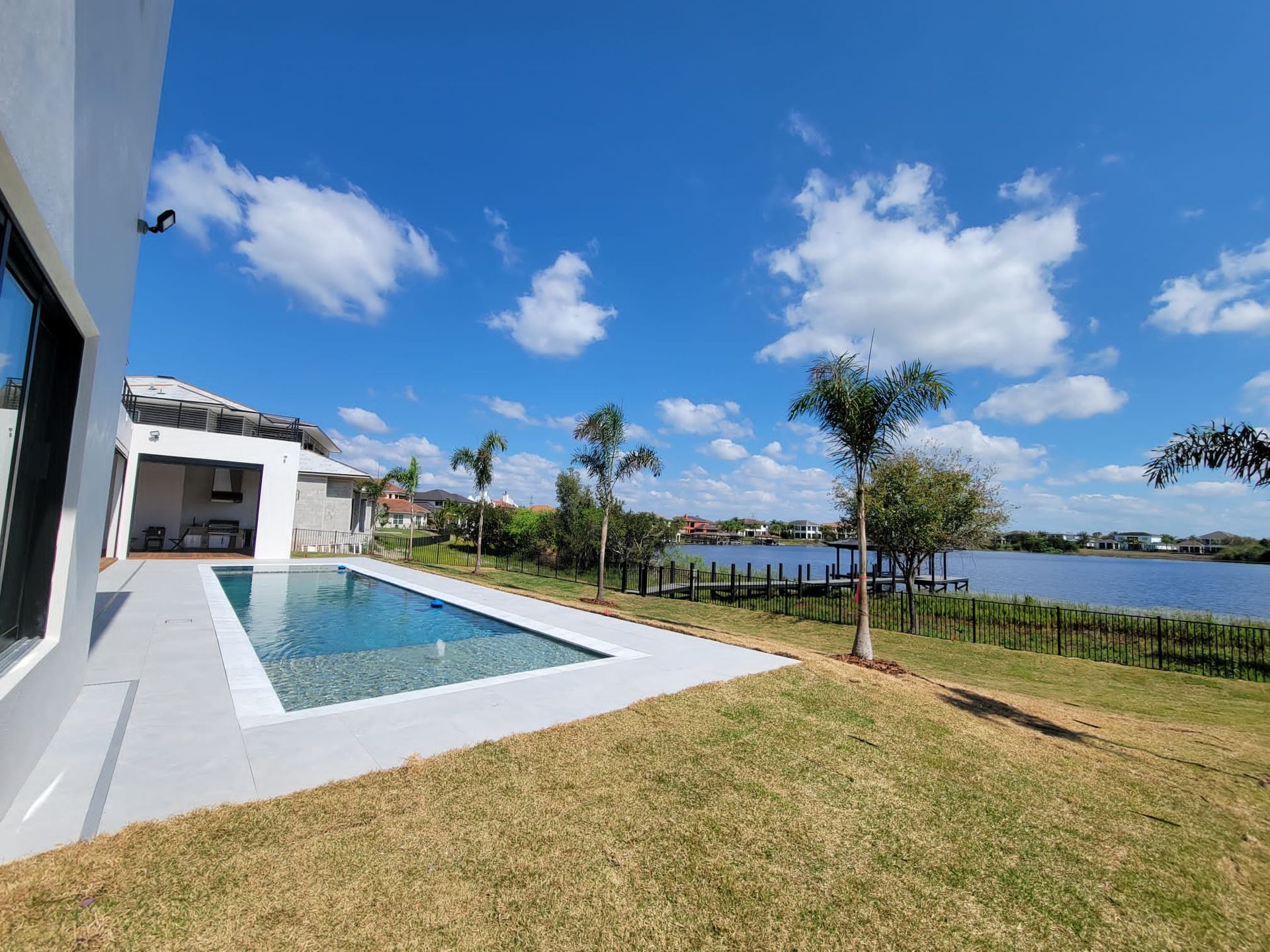 A modern house with a pool and a view of a lake under a bright blue sky with scattered clouds.