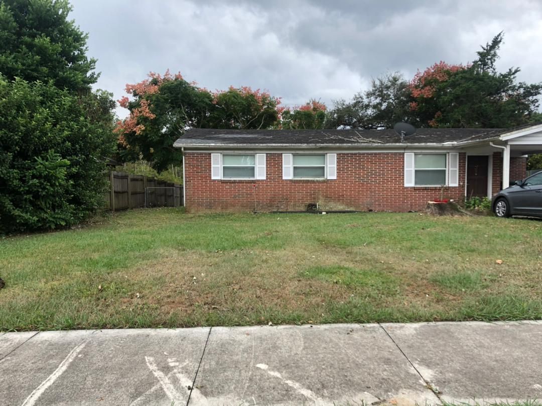 Brick house with patchy green lawn, white-framed windows, under a cloudy sky.