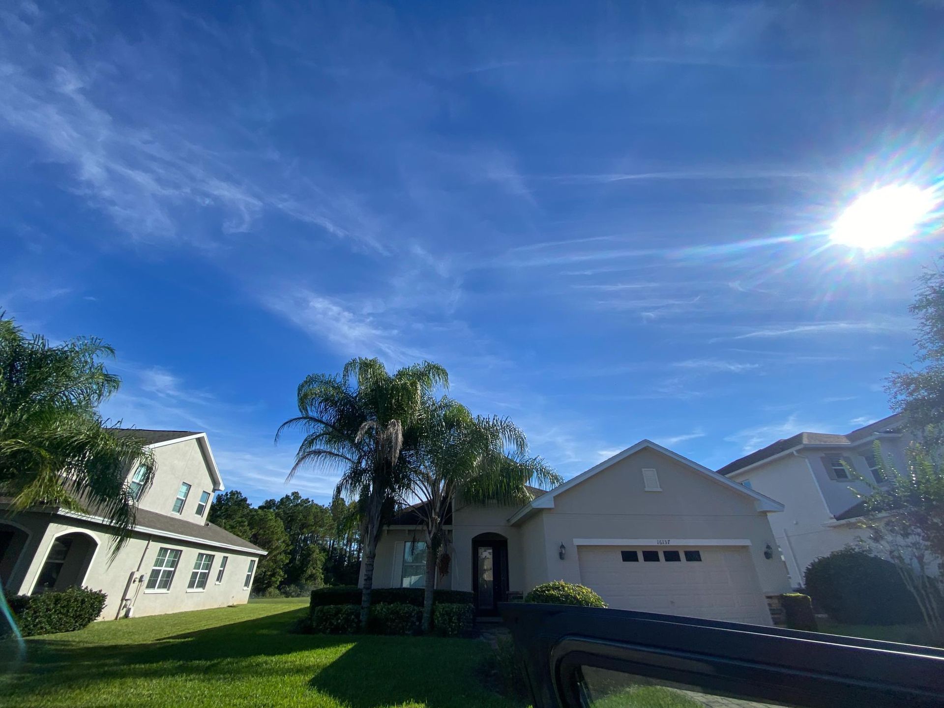 Suburban homes under a bright blue sky with wispy clouds and the sun shining.