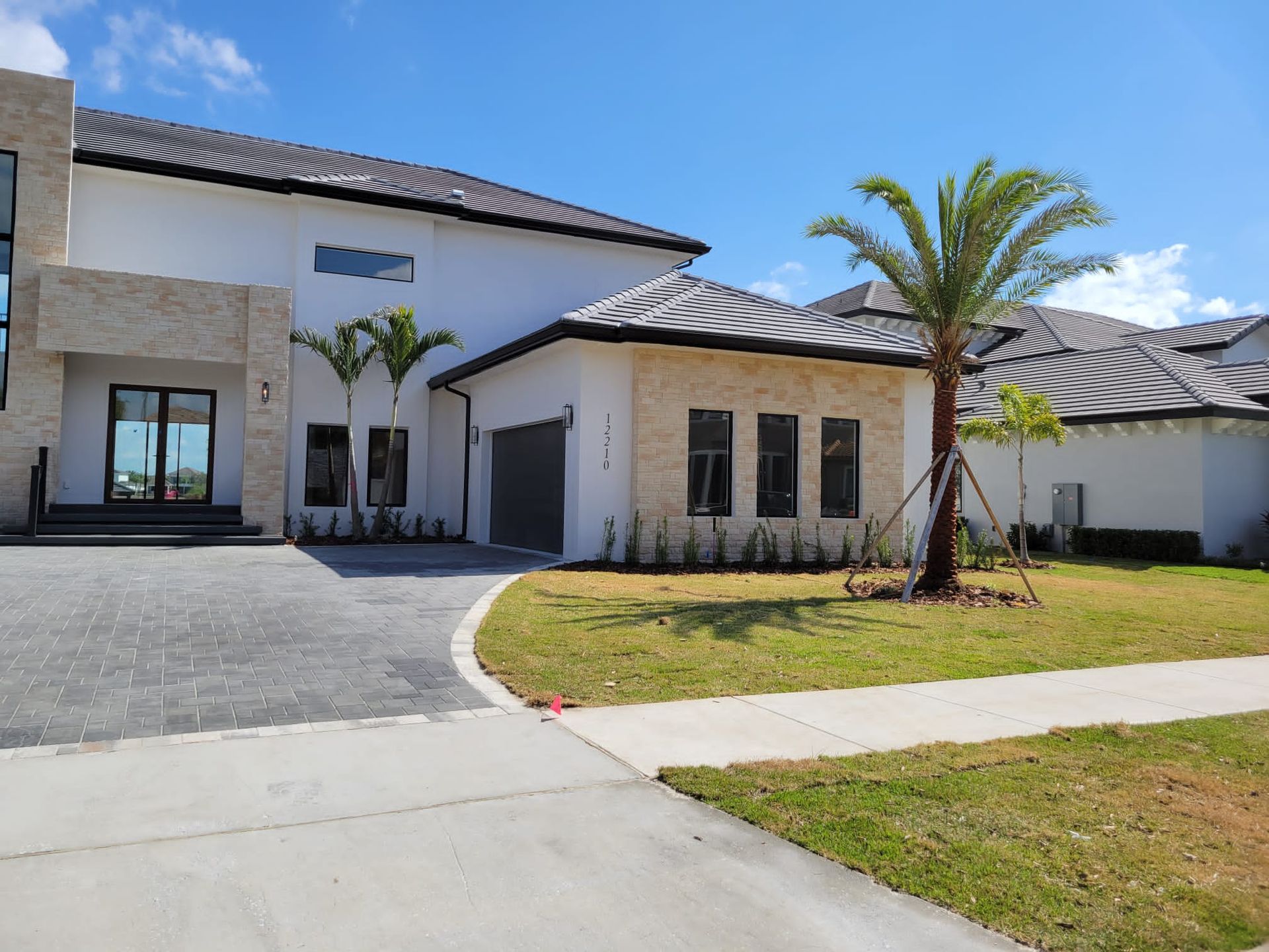 Modern two-story house with a driveway and palm trees against a blue sky.