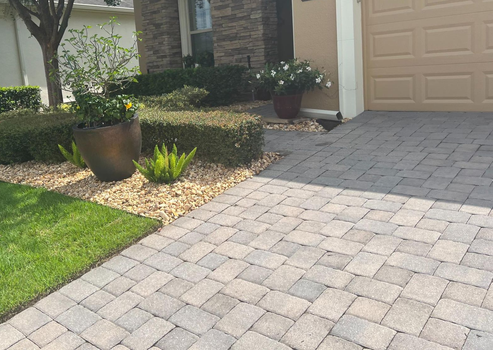 Front yard with paver driveway, green lawn, potted plants, and a garage entrance