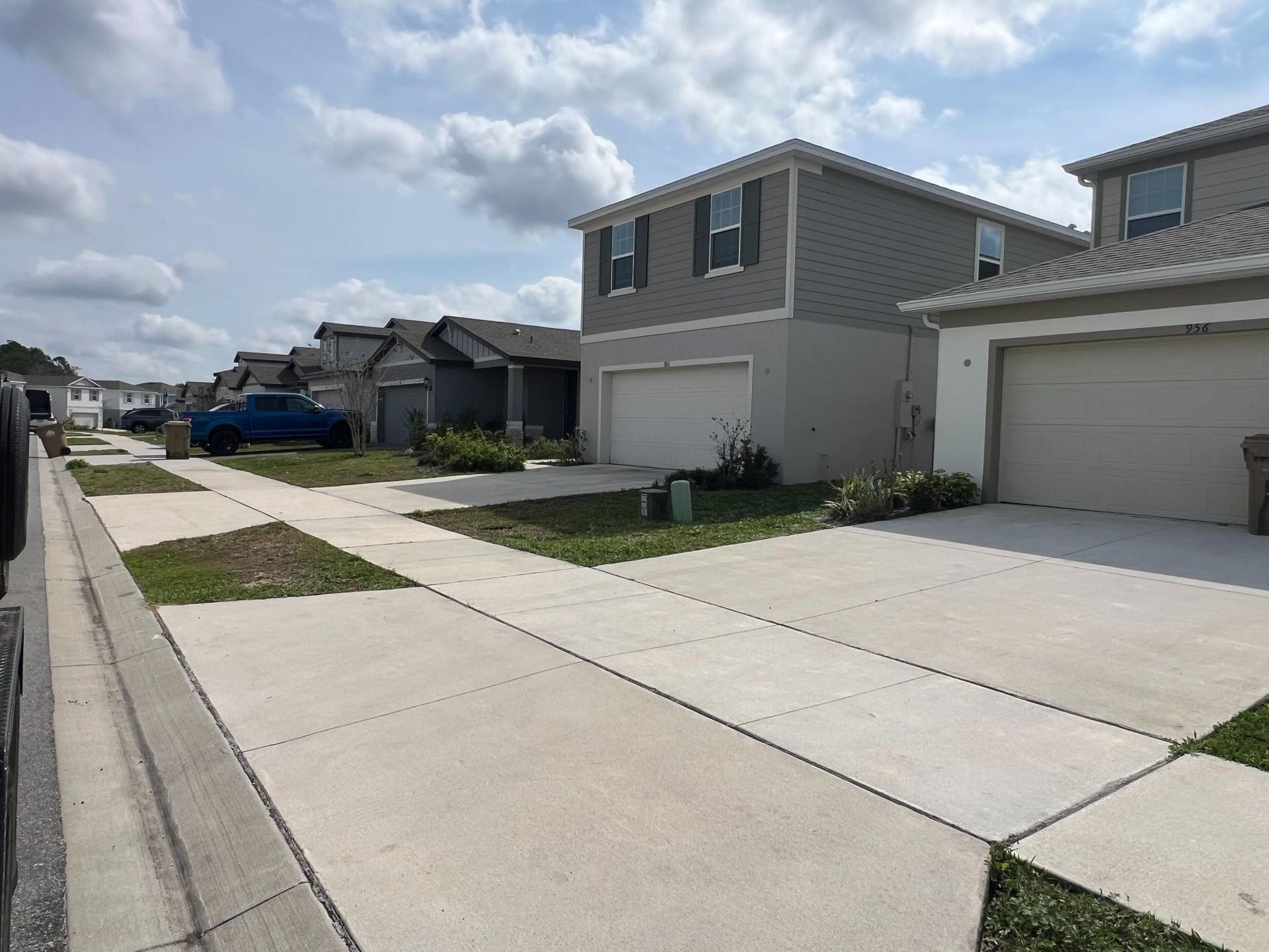 Row of two-story houses with driveways and small patches of grass. Cloudy sky overhead.