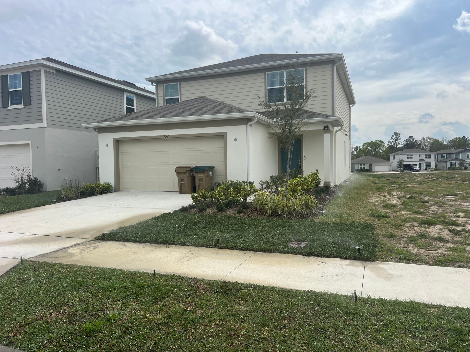 Two-story house with tan siding, a two-car garage, and a concrete driveway on a cloudy day.