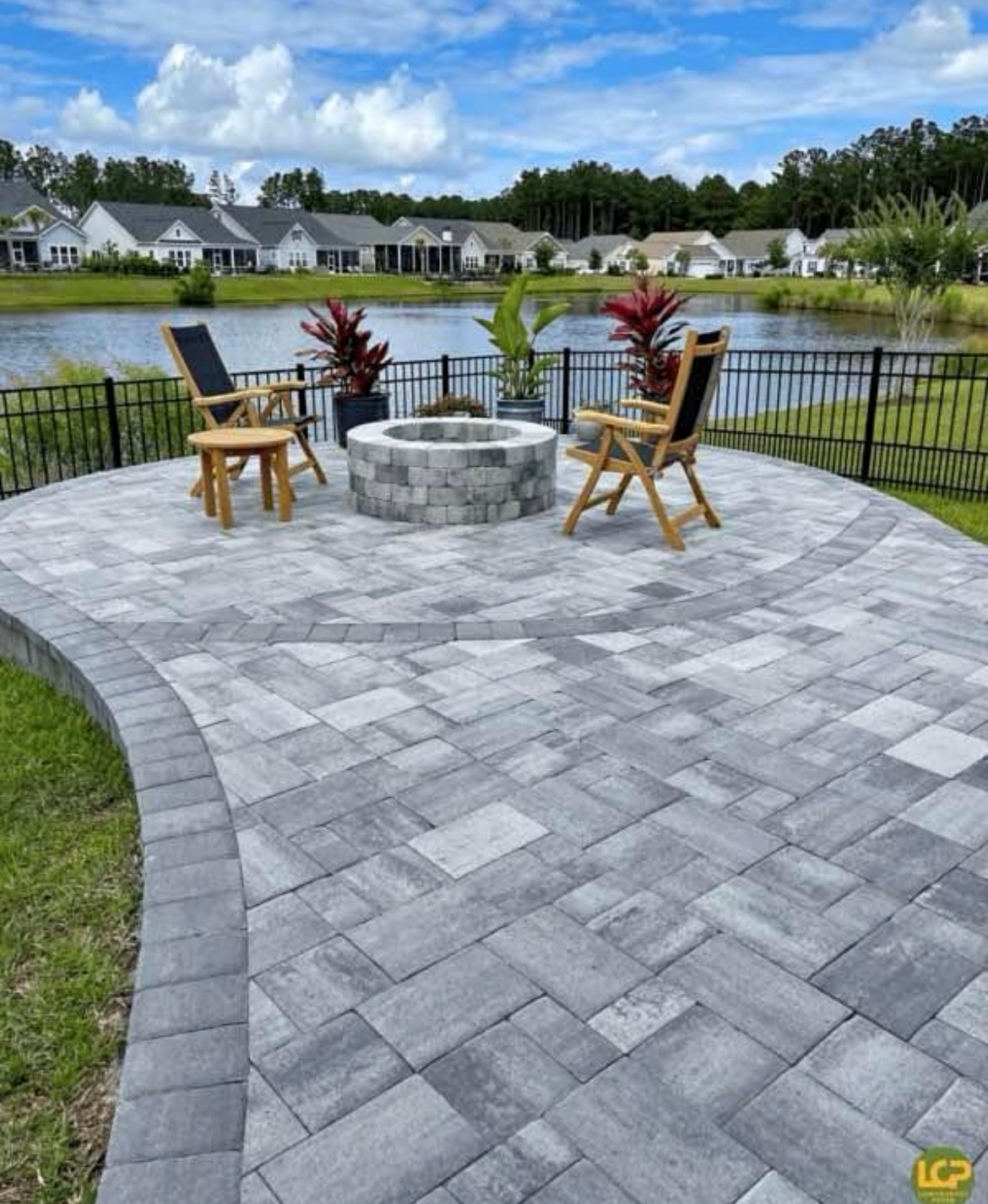 Patio with gray pavers, fire pit, lake view, and two wooden chairs.