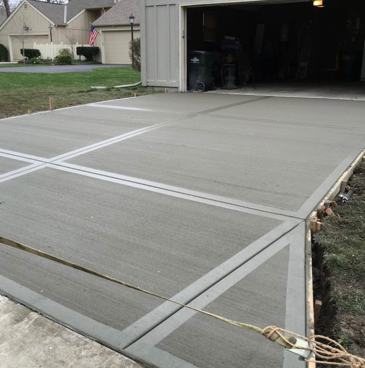 Newly poured concrete driveway with decorative gray lines near a garage.