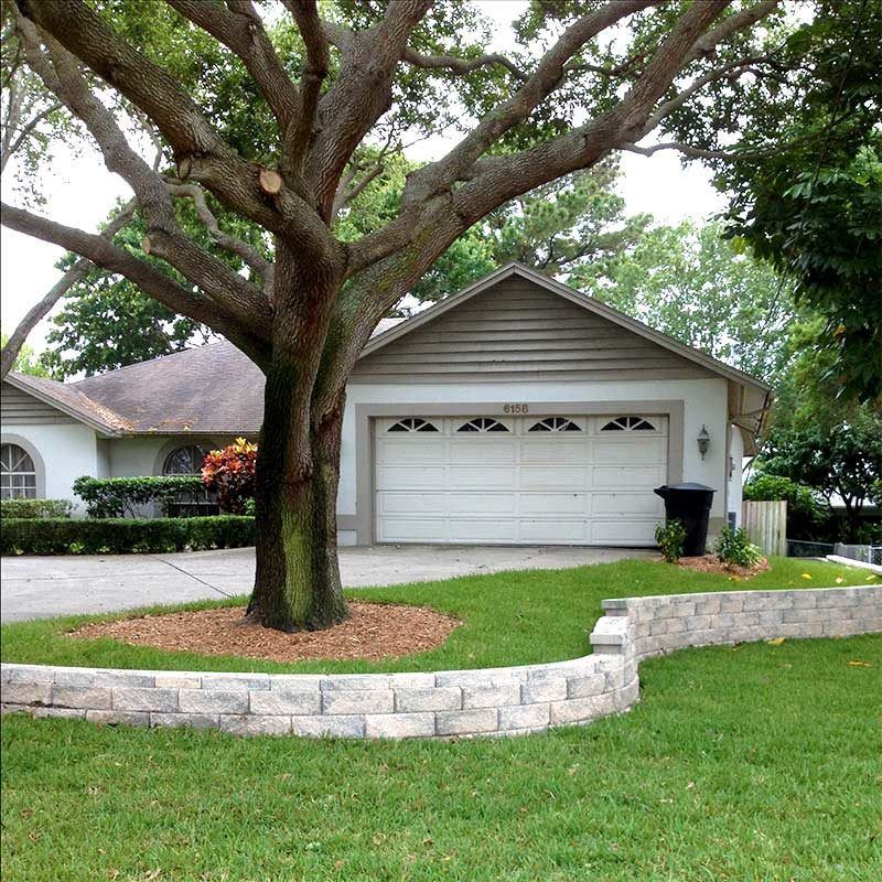 A house with a two-car garage, a tree in the yard, and a retaining wall.