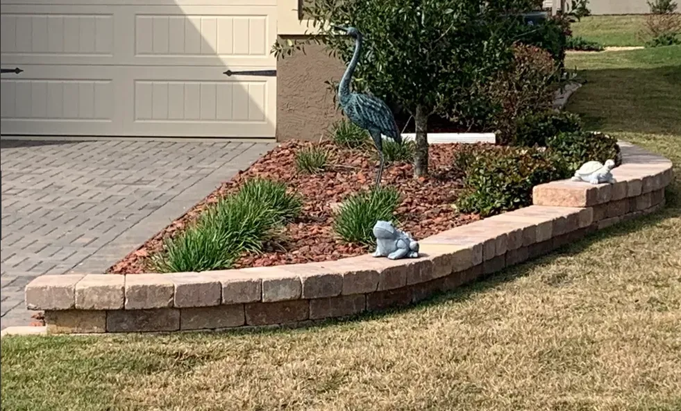 Brick-edged garden bed with mulch and plants, a few animal statues, in front of a garage.