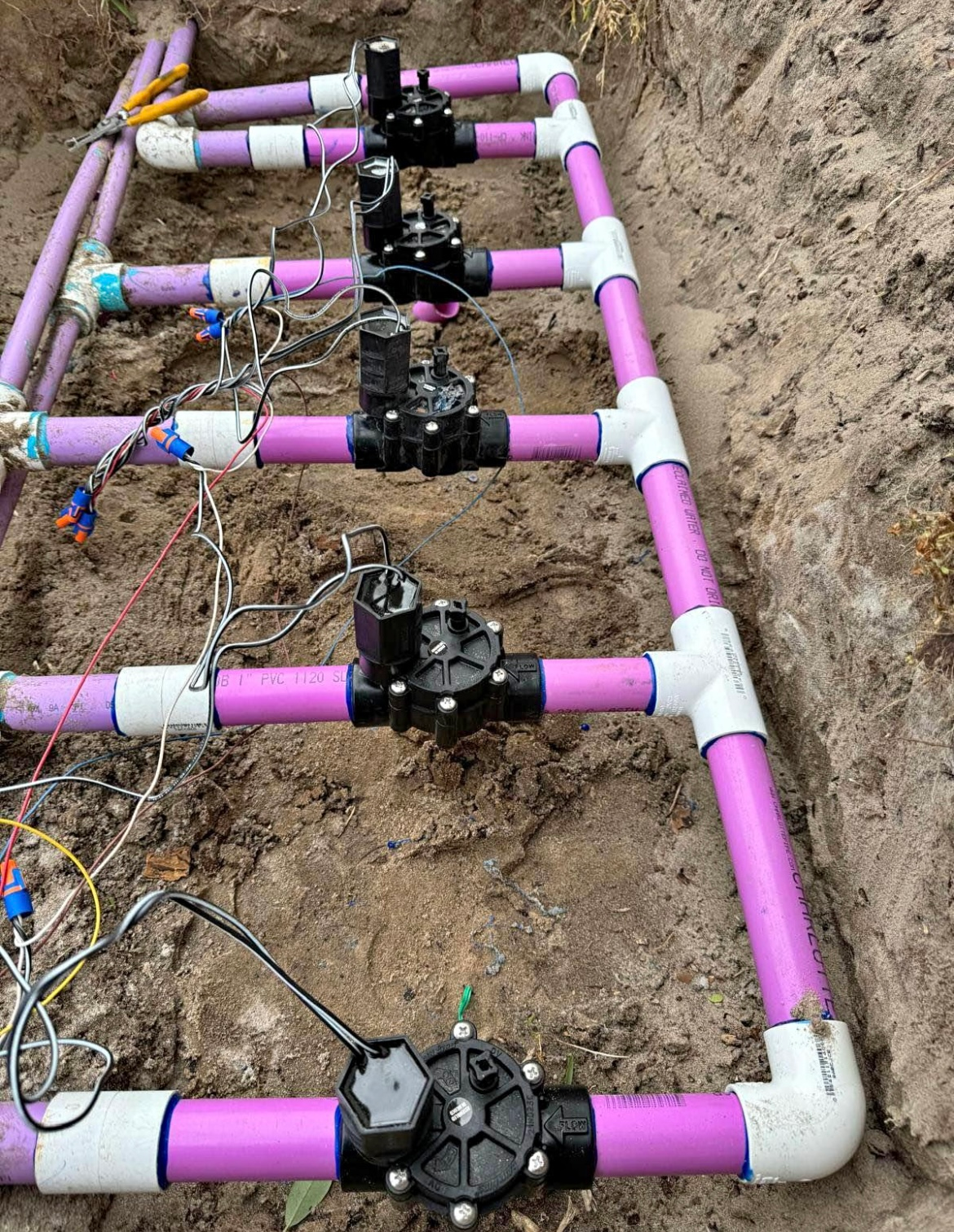 Irrigation system with purple PVC pipes and black valves, installed in a dirt trench.