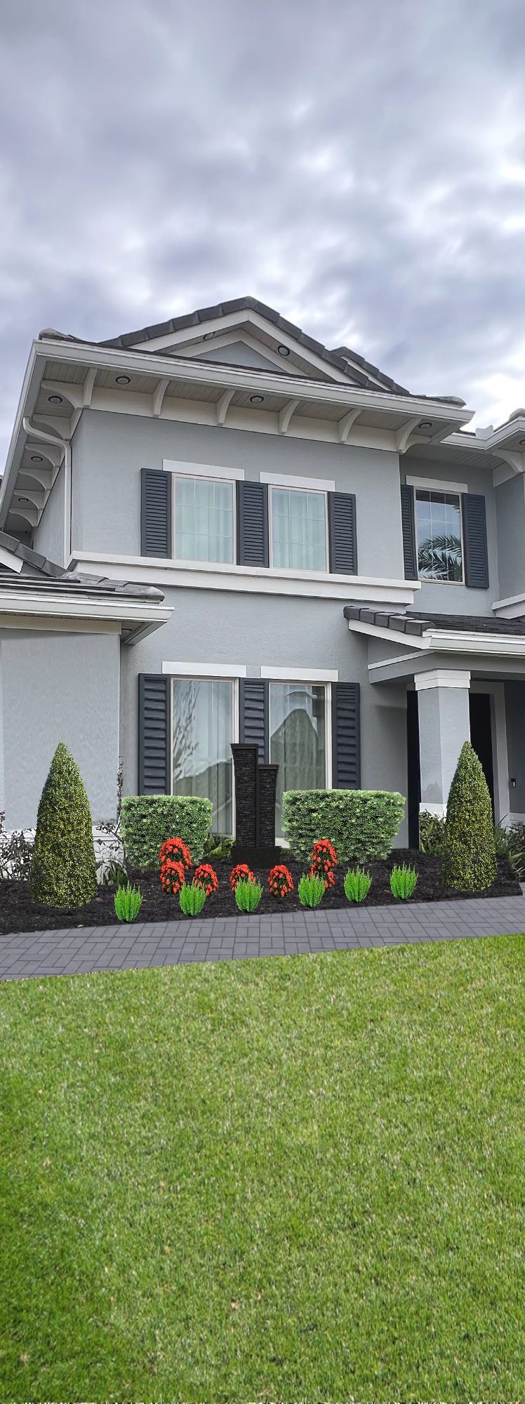 Two-story gray house with black shutters, a lawn, and a flower bed on an overcast day.