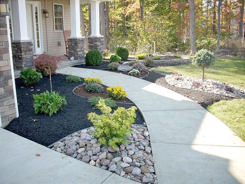 Cement walkway curves through a landscaped front yard with green shrubs and mulch.