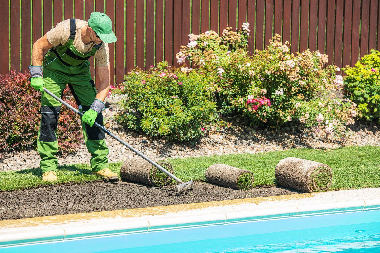 Worker trimming lawn beside a swimming pool with a string trimmer
