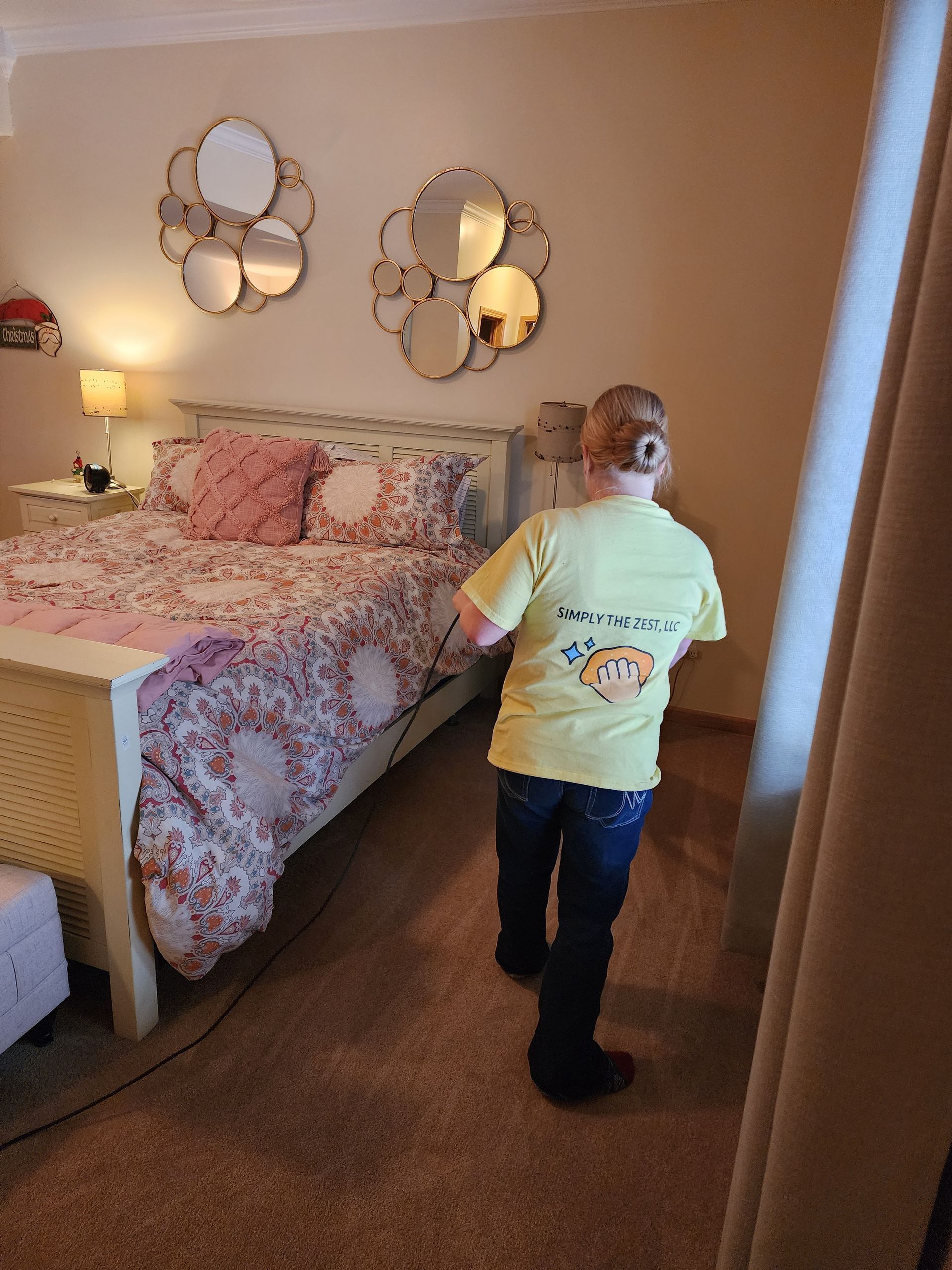 Person in a yellow t-shirt walking past a bed in a bedroom. Decorative mirrors hang above the bed.
