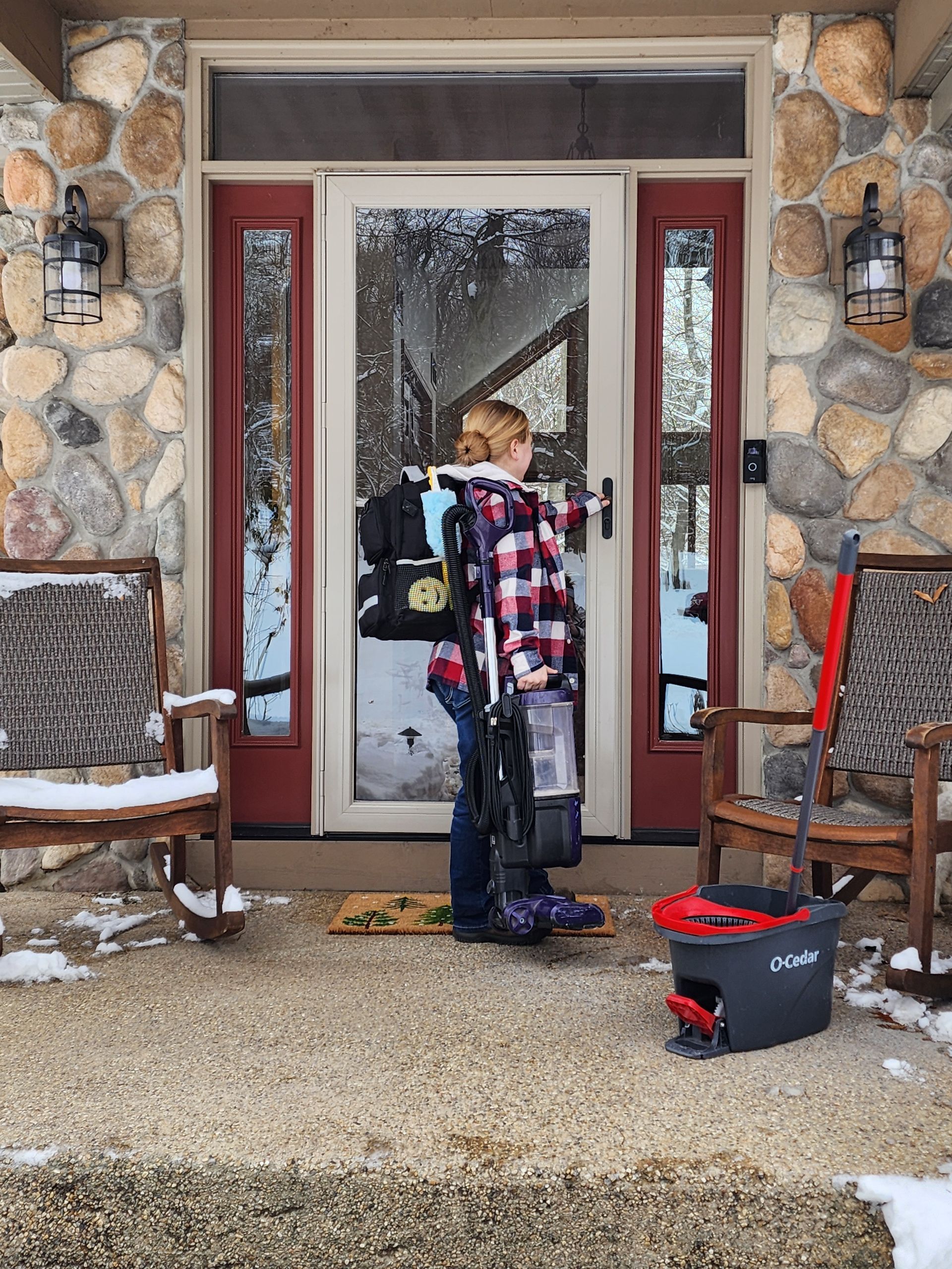 Person standing at a door, carrying a backpack and gear, snow on the porch.