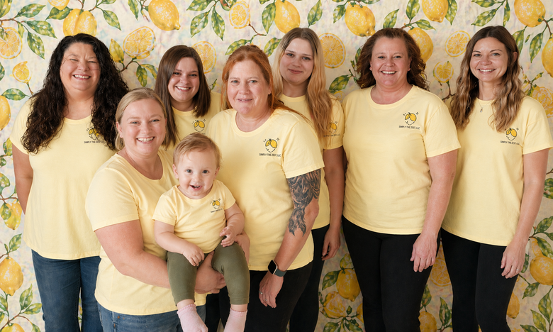 Group of women in matching yellow shirts posing indoors in front of a lemon-patterned backdrop