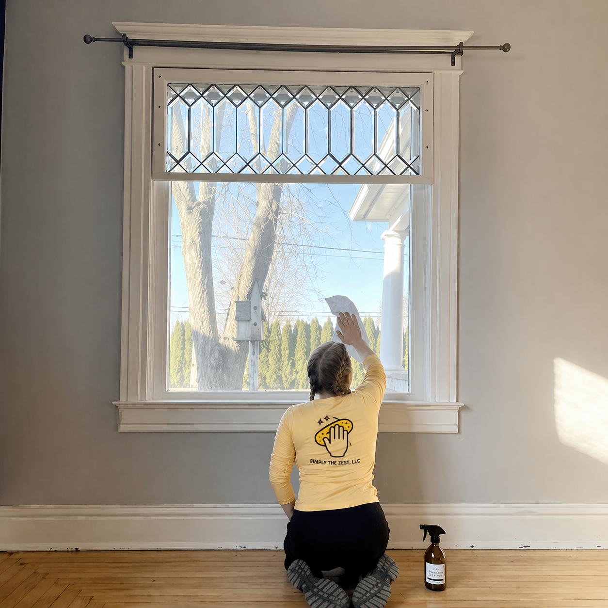 Person kneels by a window, reaching up to clean or paint the glass in a bright room.
